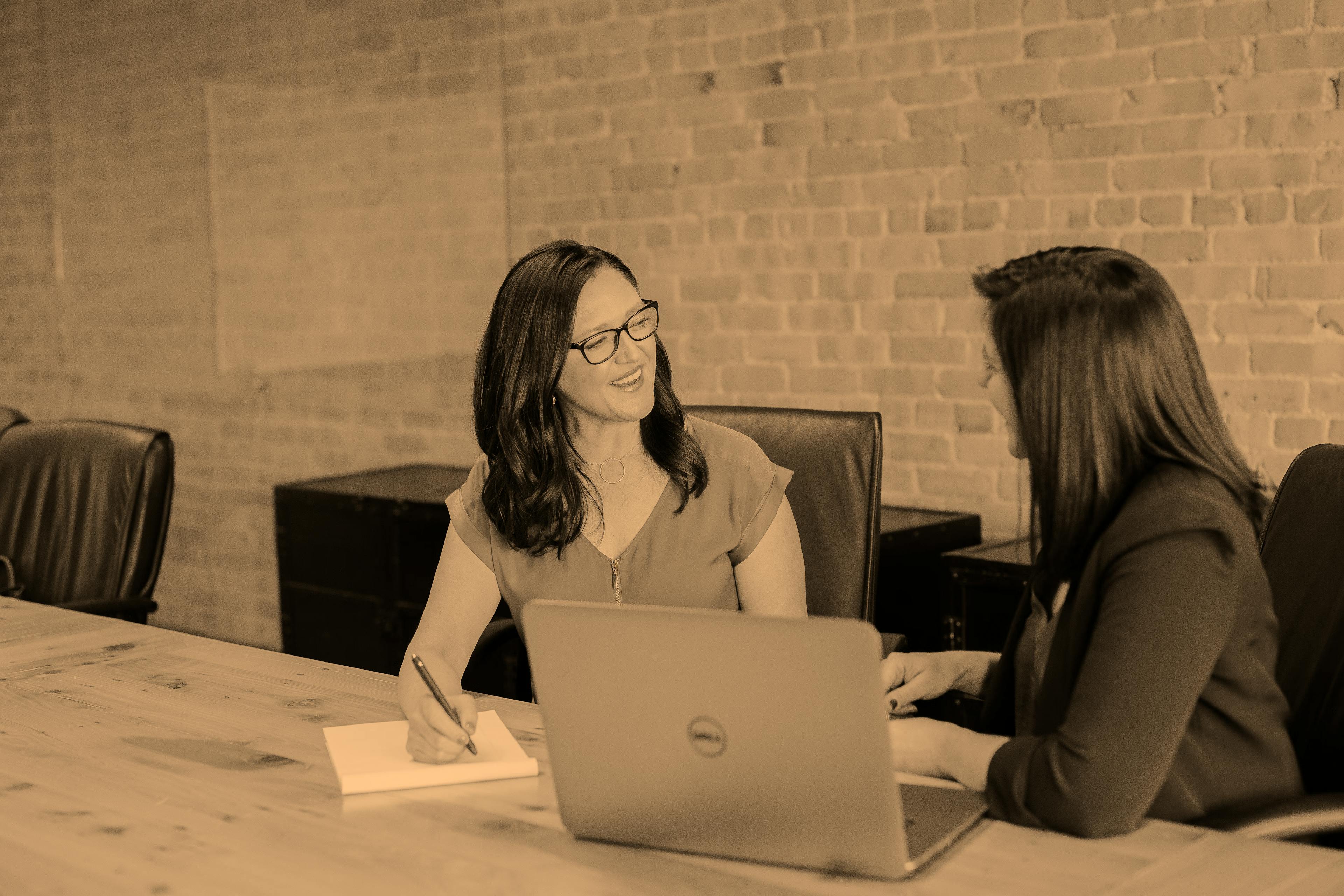 women talking in an office with a paper and a laptop in front of them.