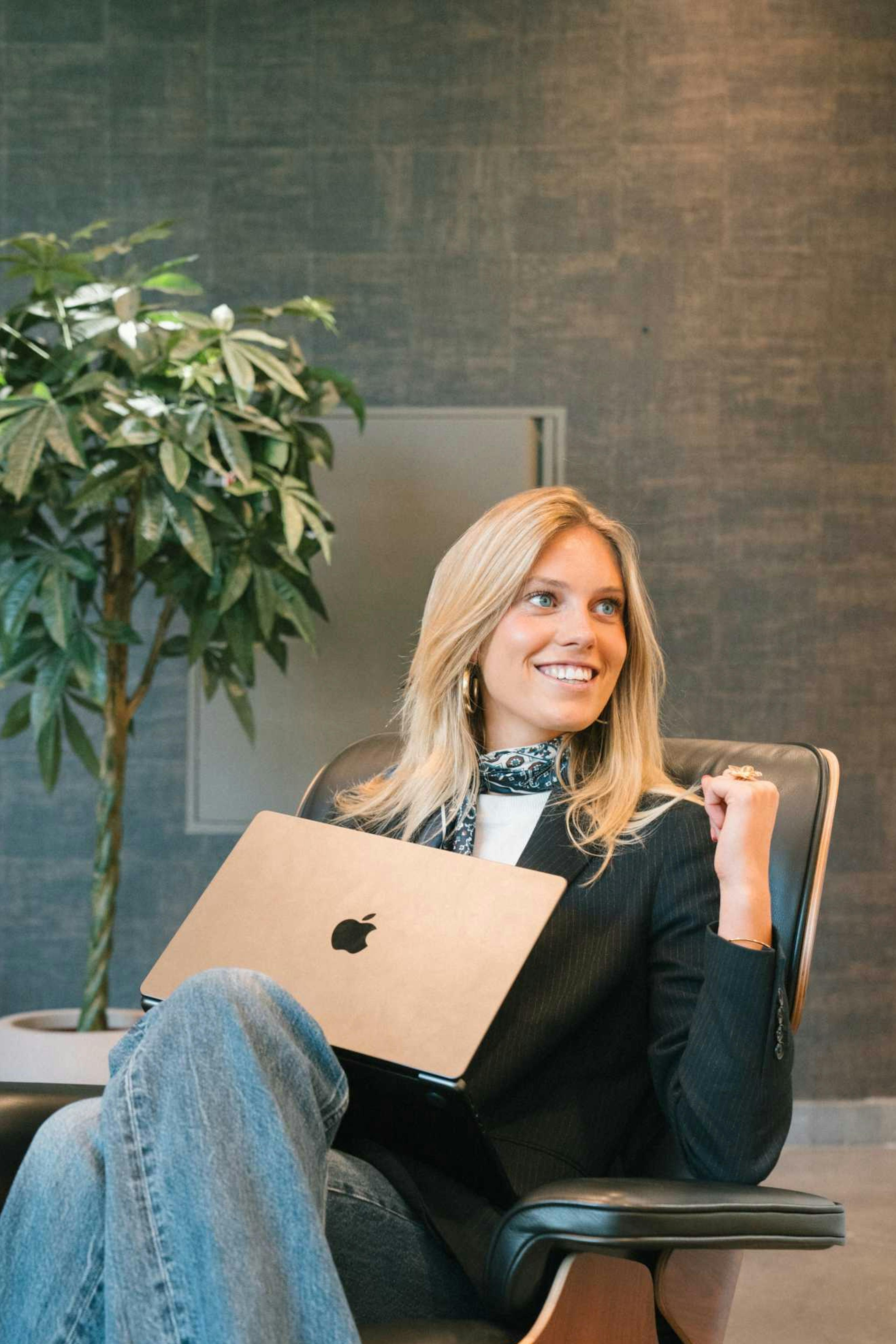 Willemijn zit in een luxe bureaustoel in de lobby van het kantoor van Elevation Group met een laptop op schoot. 