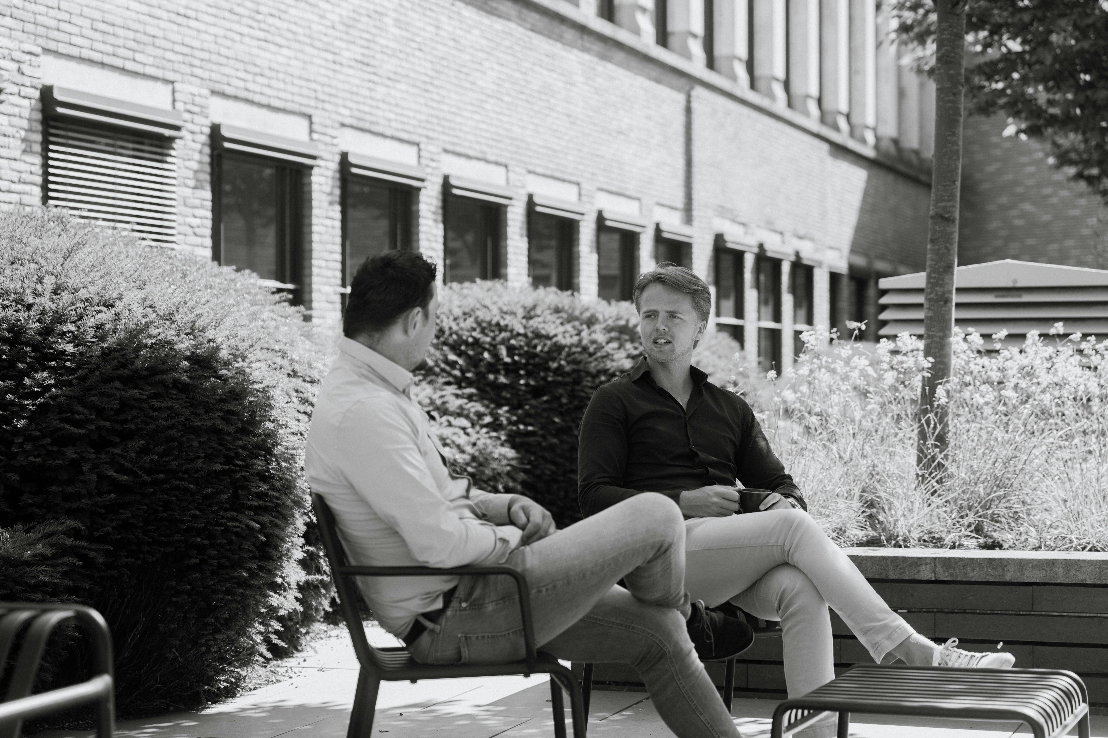 Collega's in gesprek in binnentuin kantoor zwart/wit.