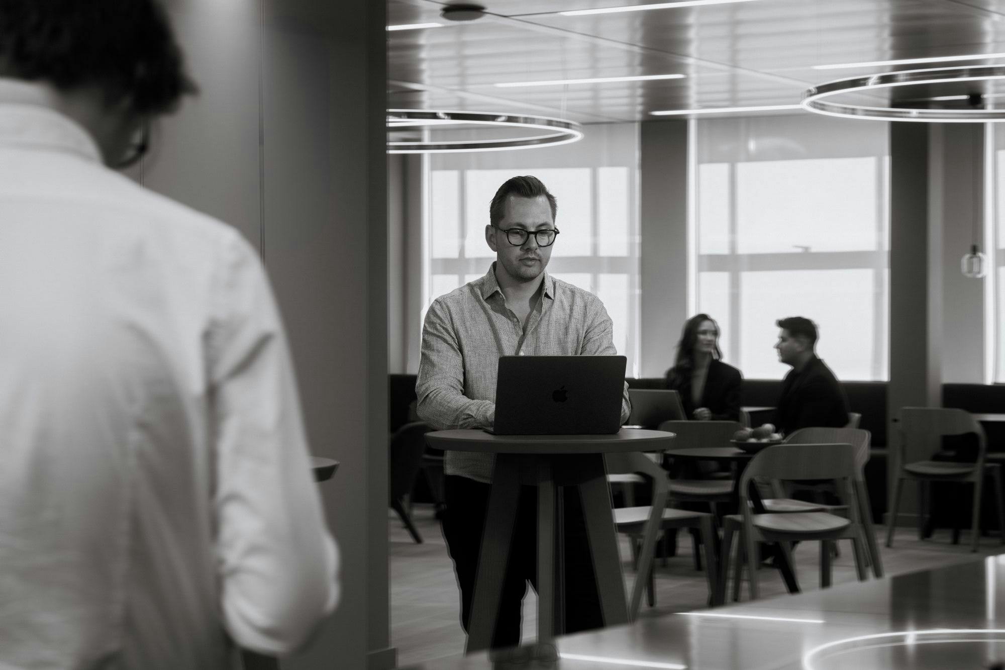 Zwart-wit afbeelding van werkende man achter laptop in de aula van Elevation Partners.