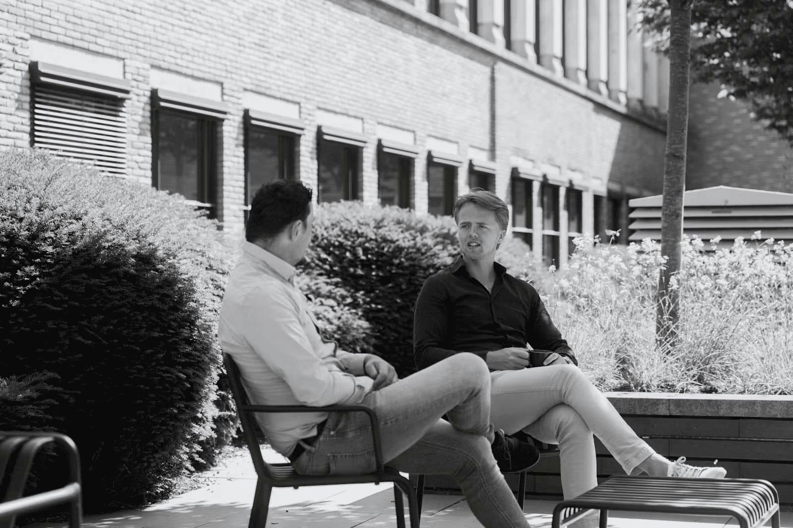 Zwart wit afbeelding van medewerkers van Elevation Partners in gesprek in de binnentuin.