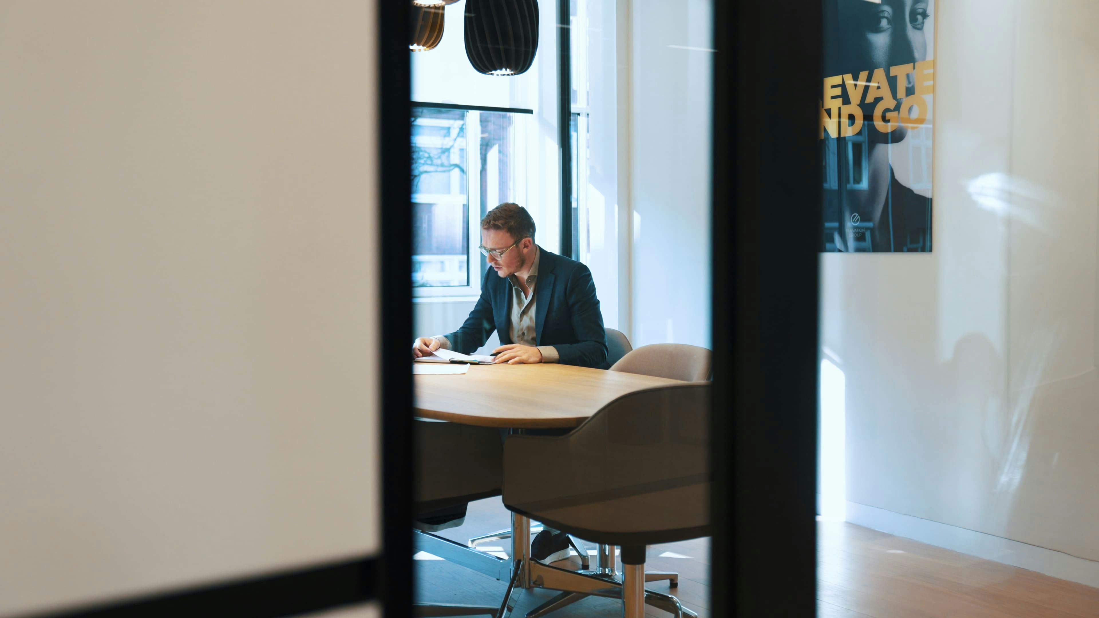 Medewerker van Elevation Partners die geconcentreerd iets leest in vergaderruimte.