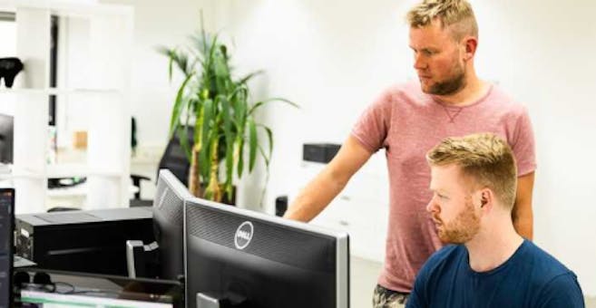 A standing developer pointing at a screen from behind a sitting developer