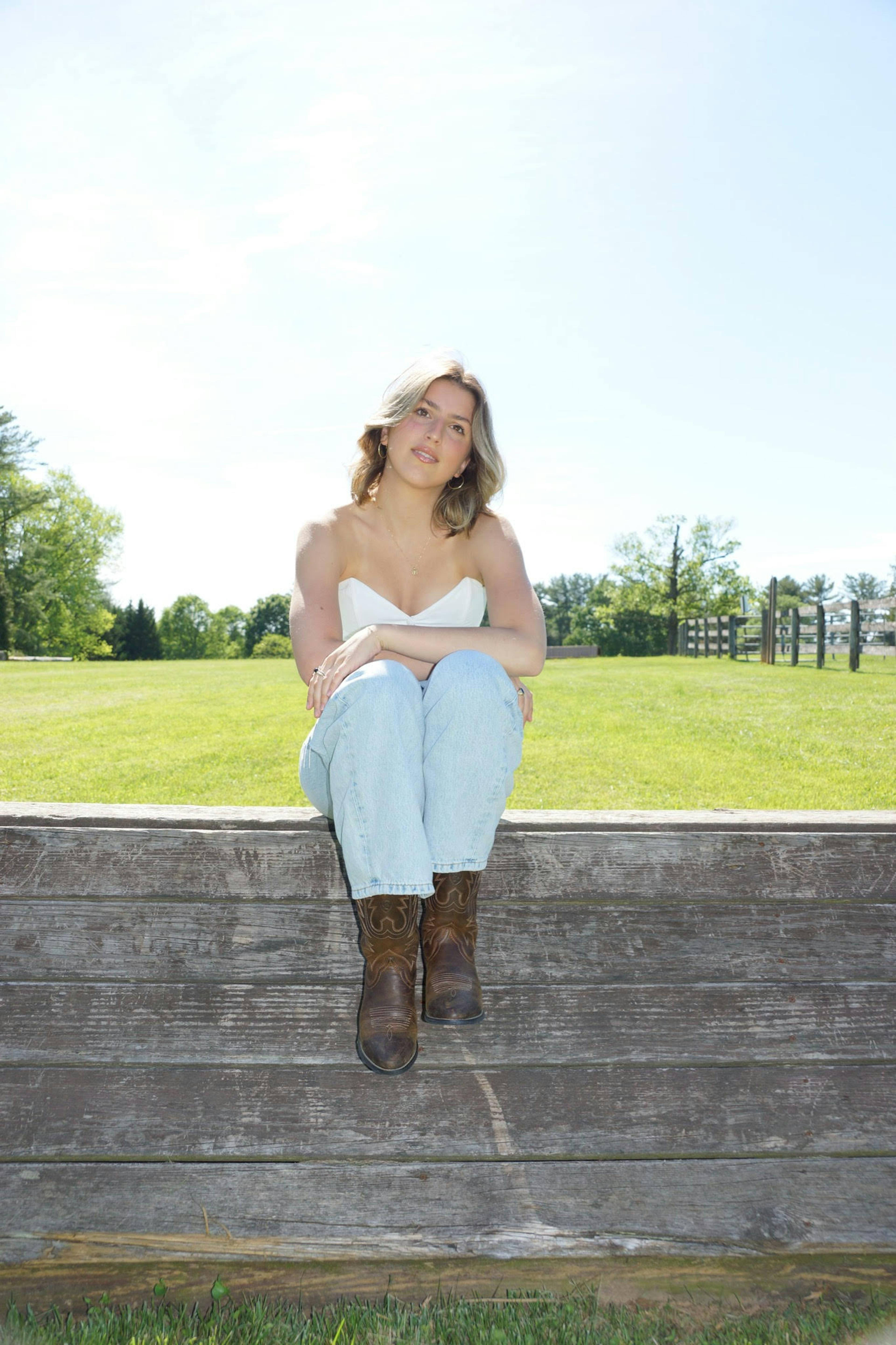 Elizabeth Young sitting on a wooden wall with trees in the background
