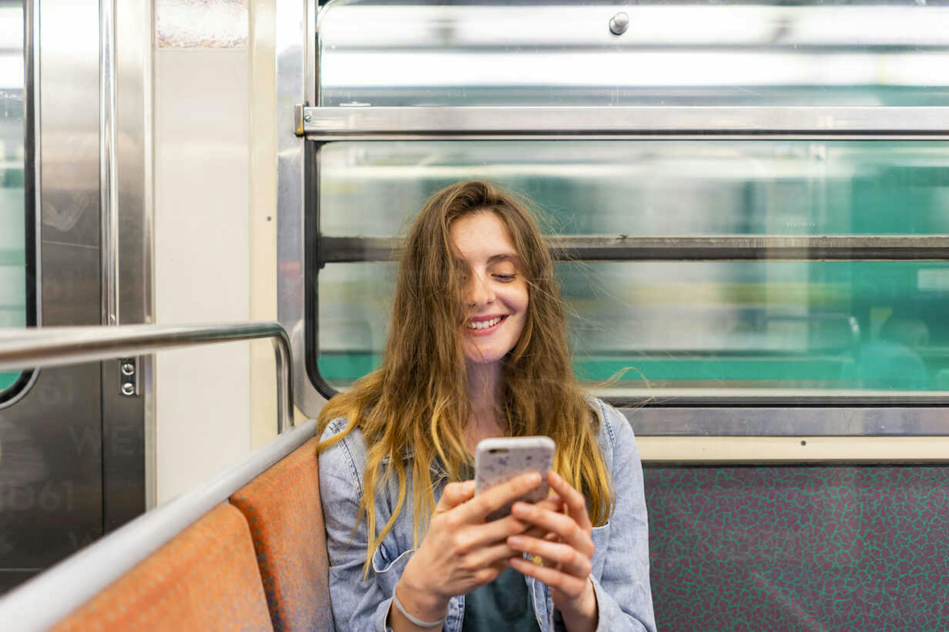Femme sur son téléphone qui sourit dans le metro