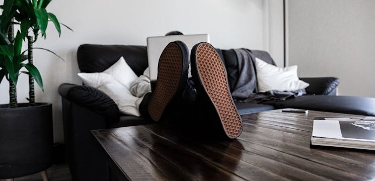 Man sitting on couch behind laptop with feet on the table