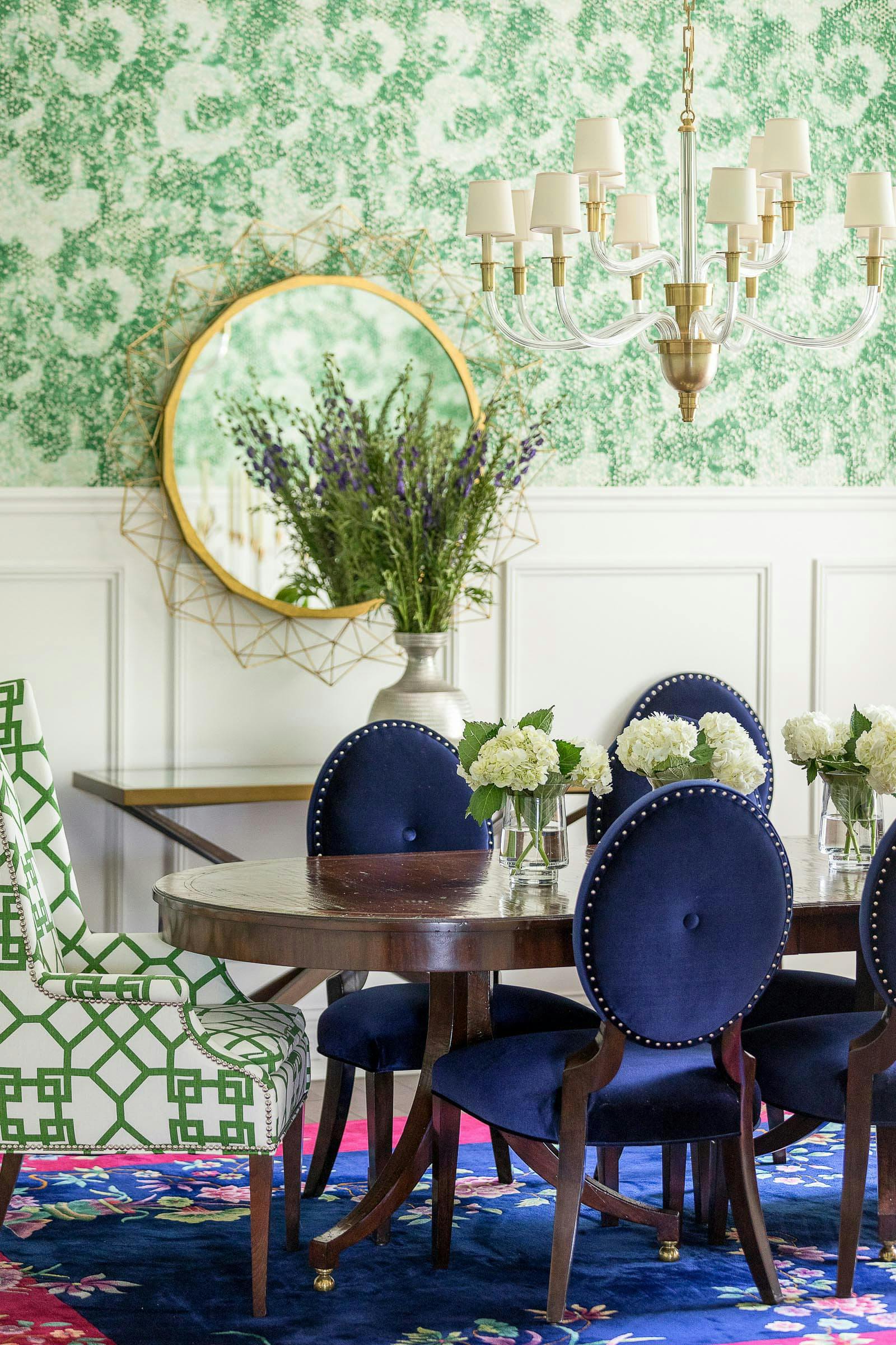 dining with with green wallpaper, wainscoting, blue velvet chairs, gold mirror and chandelier