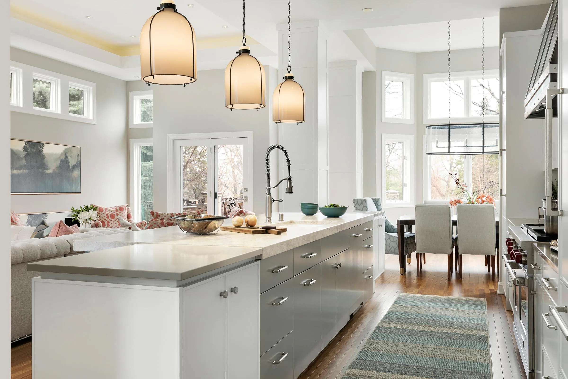 Kitchen island featuring a mix of finishes with gray and white cabinetry, quartz and quartzite countertops in two different thicknesses,  bronze pendant lighting, and white bronze cabinet hardware.