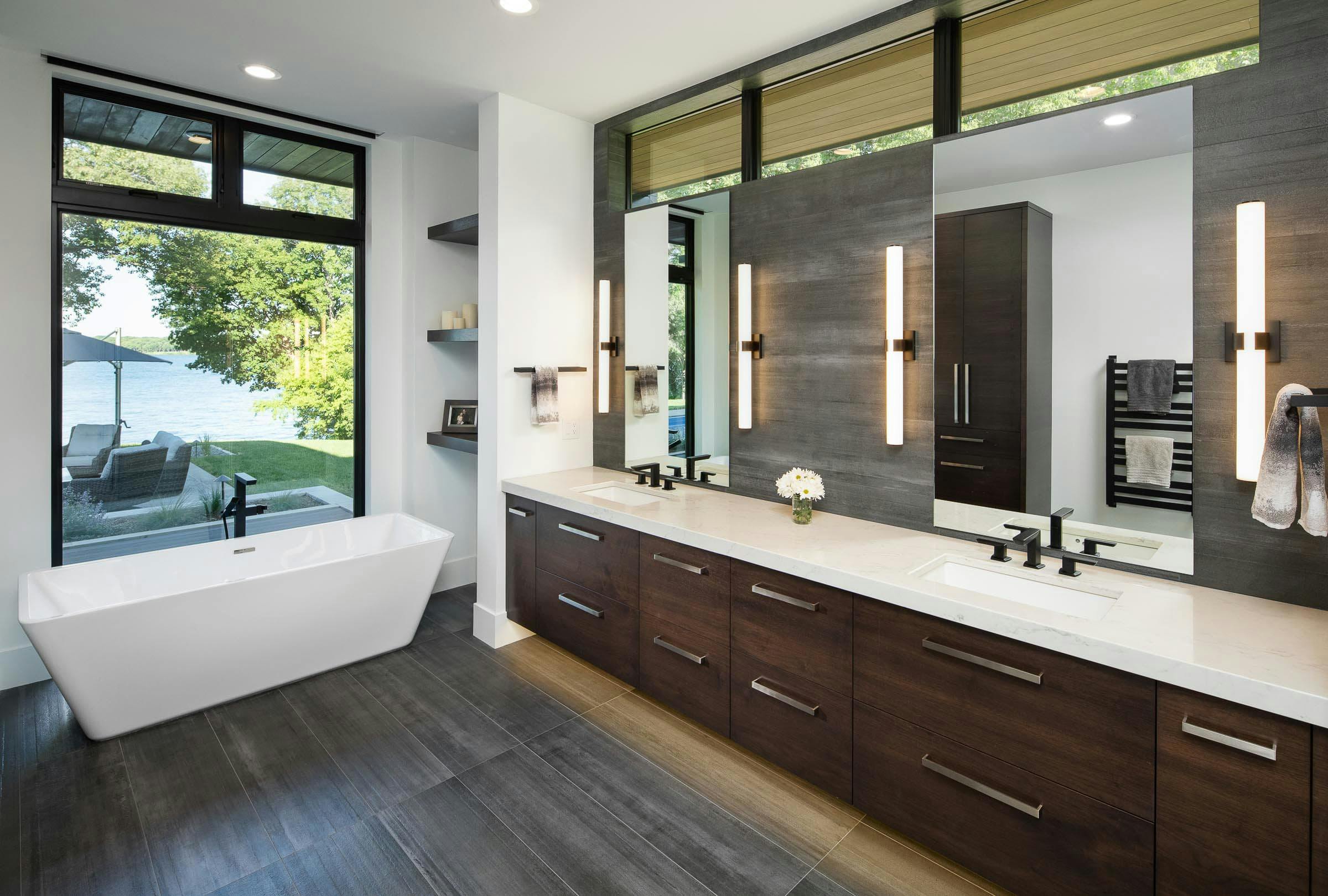 bathroom with tall windows, dark floors and walnut vanity with white top and black plumbing fixtures