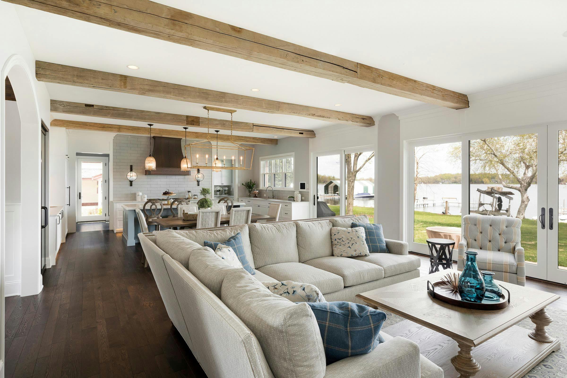 open concept with exposed beams, large sectional in living, kitchen in the background