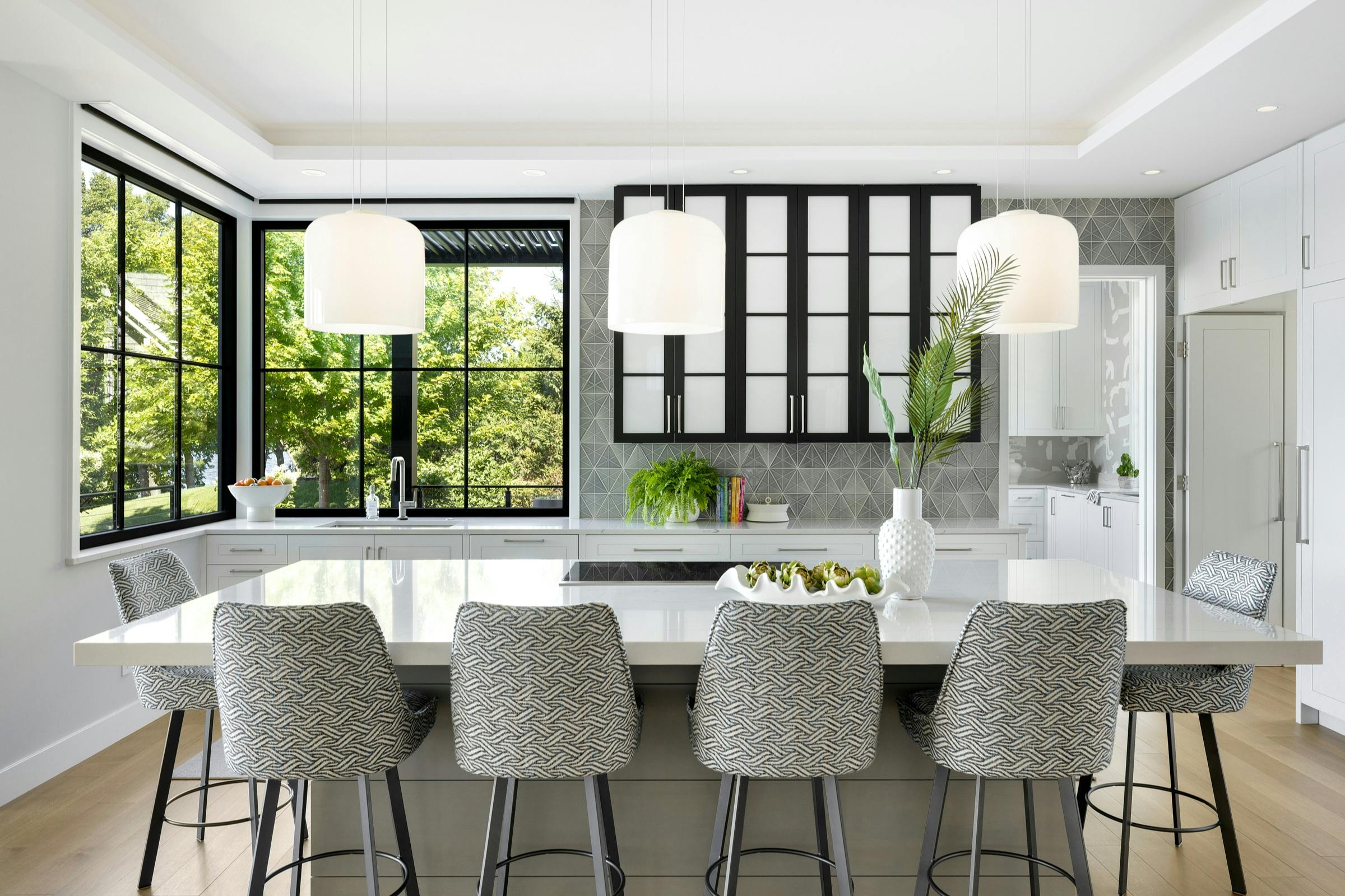 Black and white kitchen design with warm gray island and frosted glass upper cabinets in Lake Minnetonka home