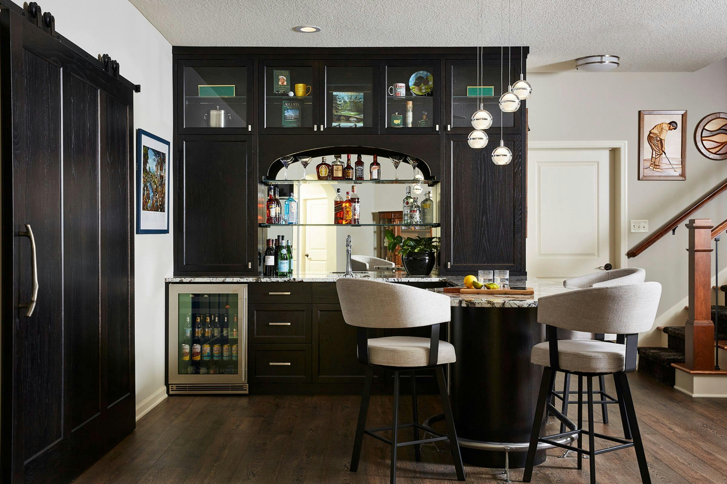 dark cabinetry used in an elegant lower level home bar design with seating and light fixture