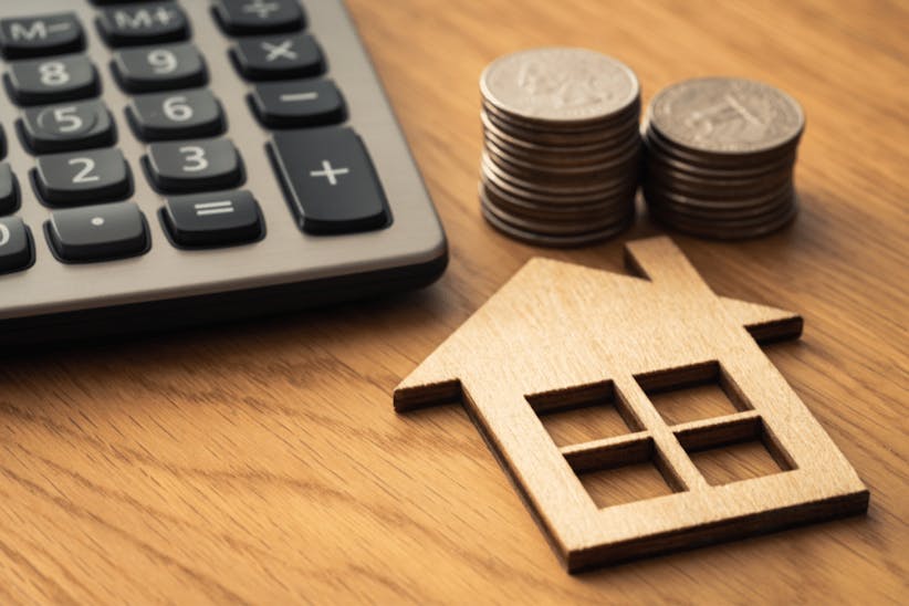 a wooden house, coins and calculator on a table