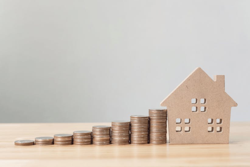 pile of coins leading to a wooden house on a table