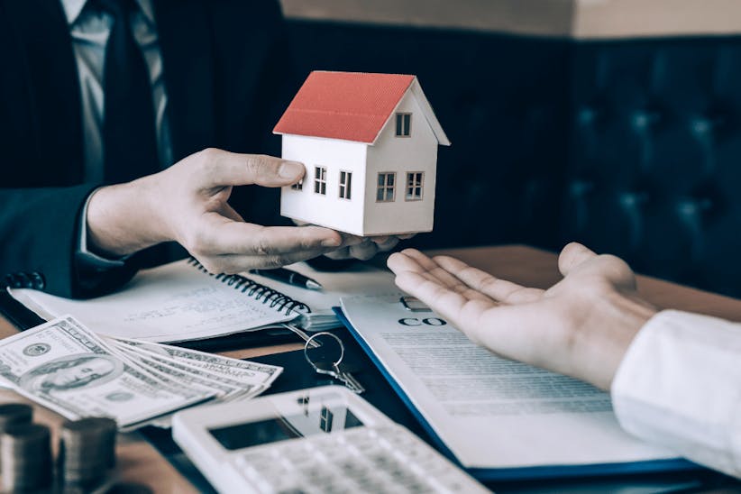 An arm holding a model of a wooden house
