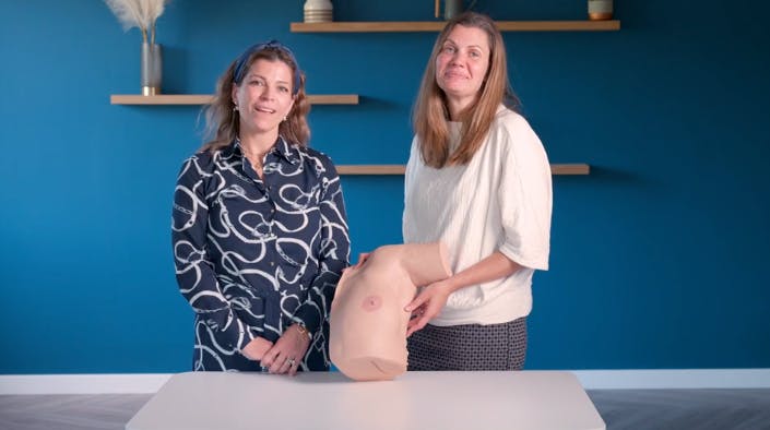 Two female surgeons posing with artificial breast exam model 