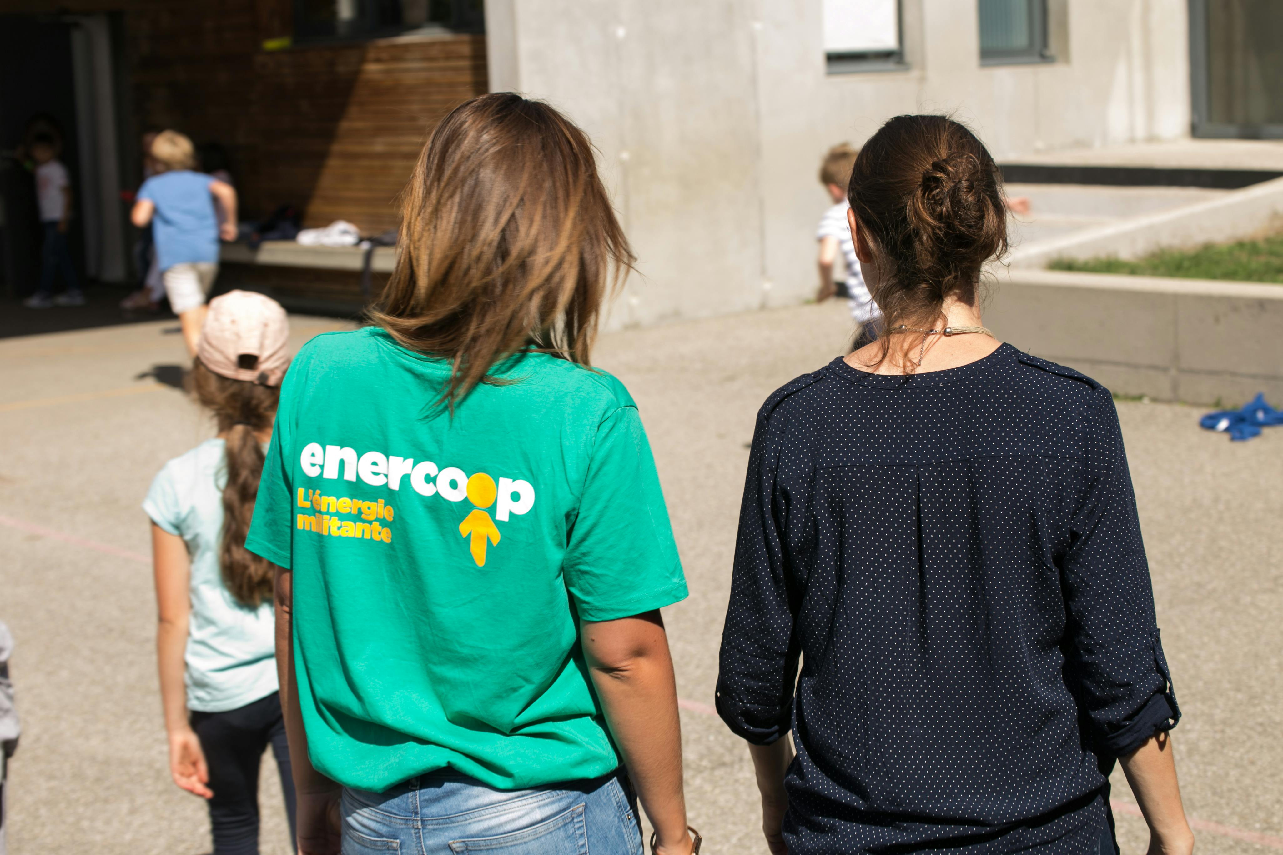 Deux femmes de dos dans une école au sein d'une collectivité. L'une avec un t-shirt vert Enercoop.