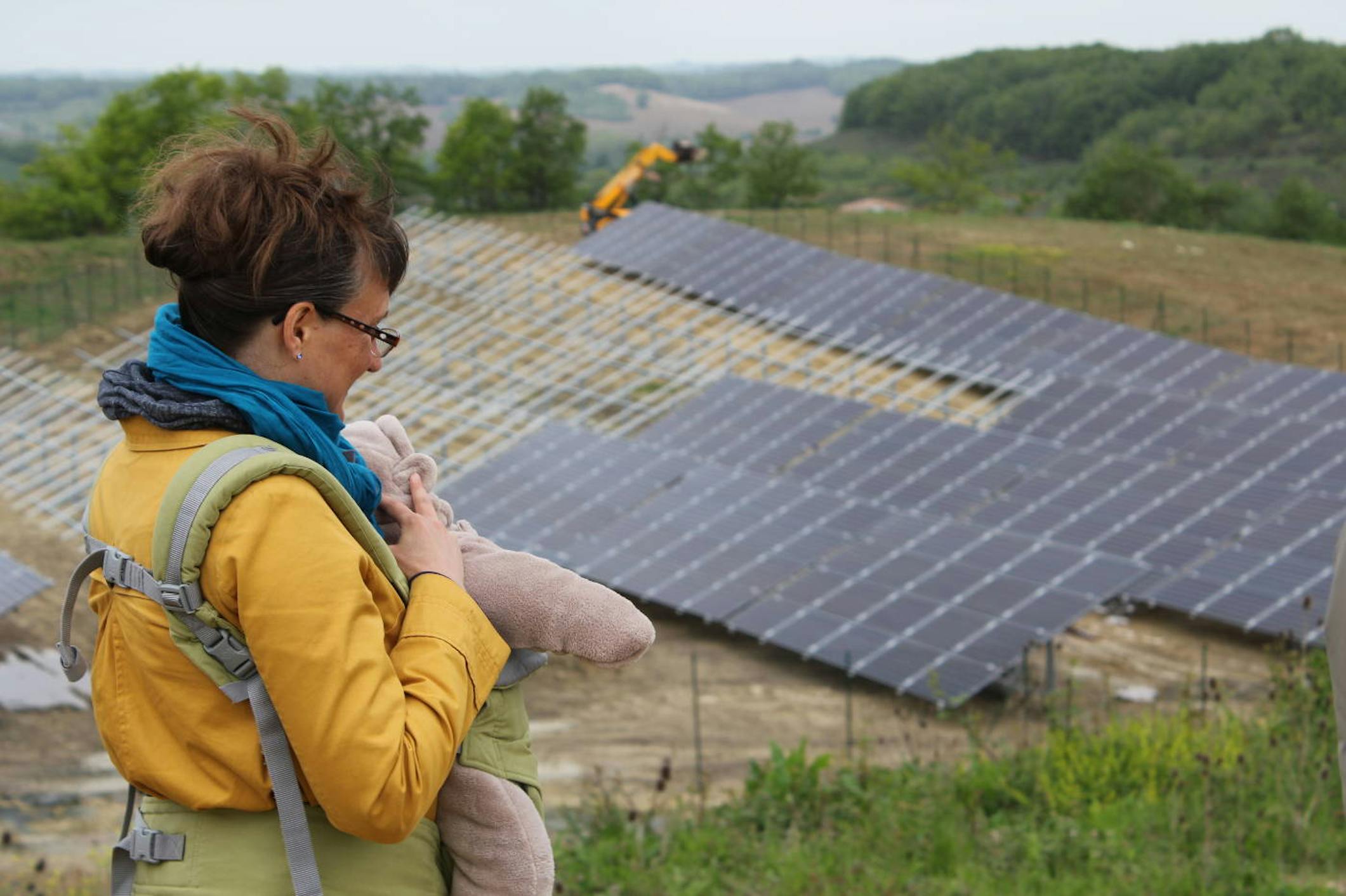 Femme portant un bébé devant un parc solaire d'Enercoop Midi-Pyrénées en construction 