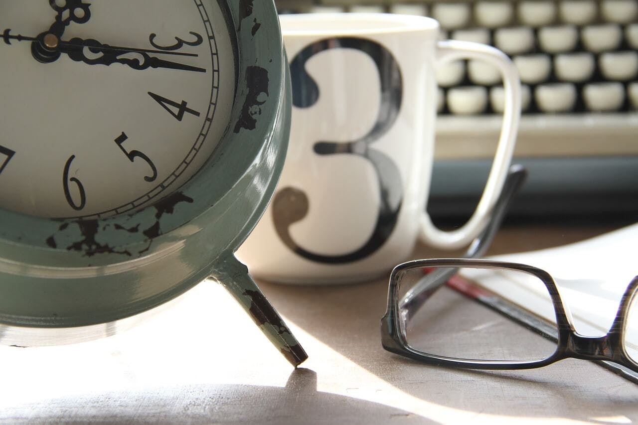 A clock, mug with number 3, glasses, and a keyboard.