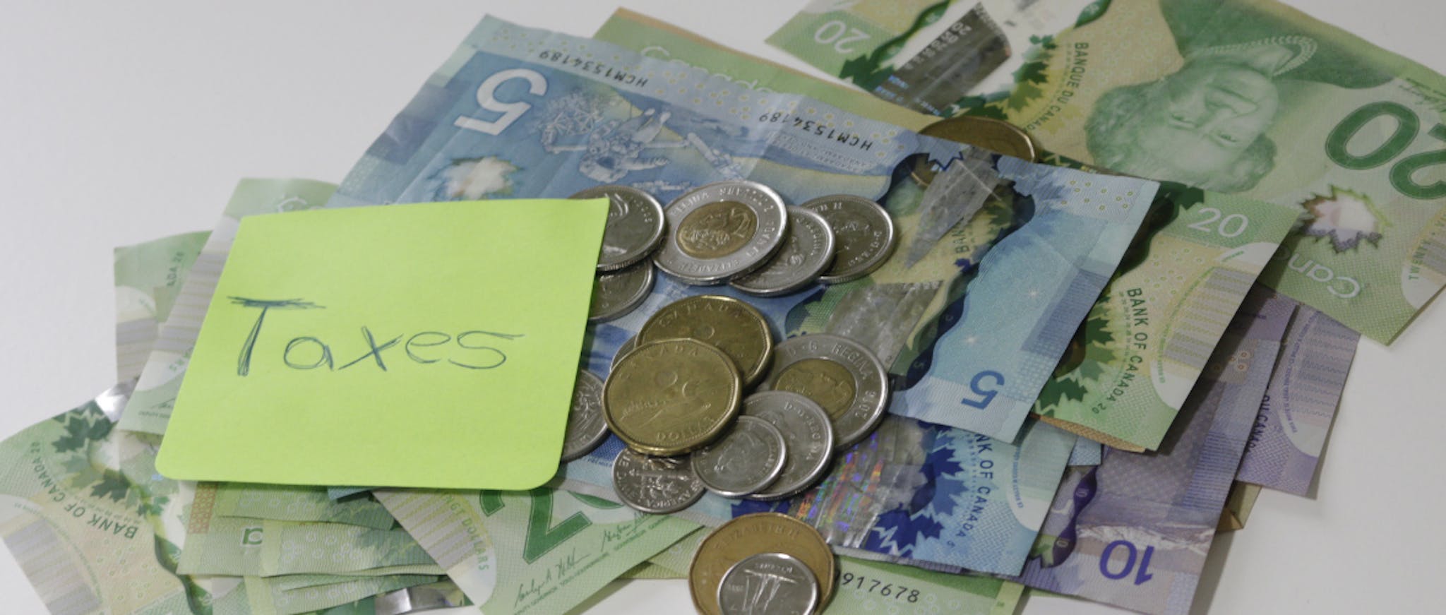 Picture of Canadian money with a note that has 'Taxes' handwritten on it 