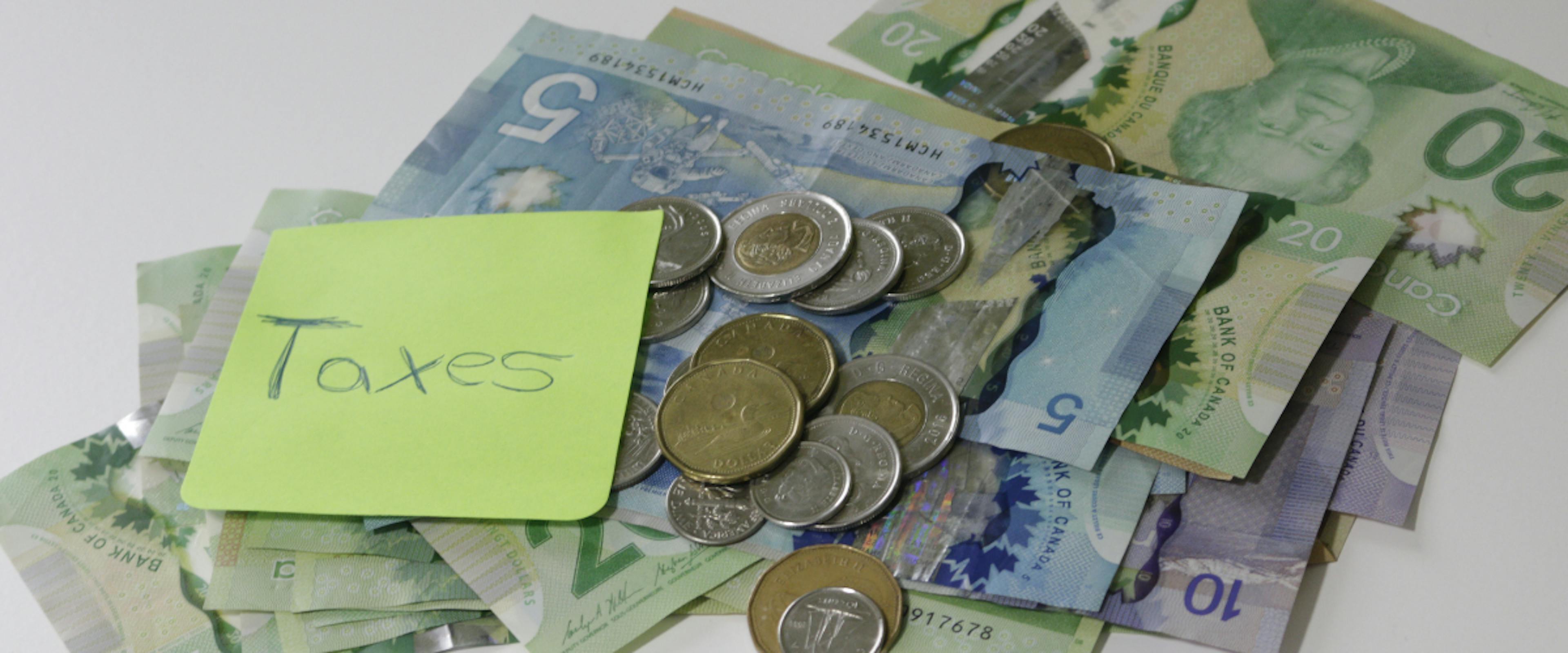 Picture of Canadian money with a note that has 'Taxes' handwritten on it 