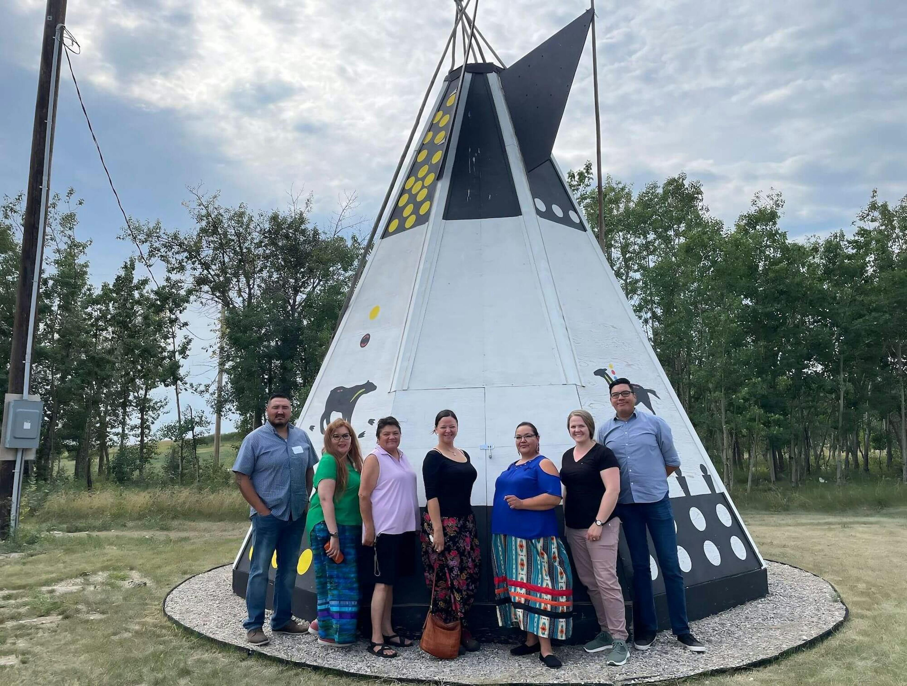  A smiling team stands outside a tipi