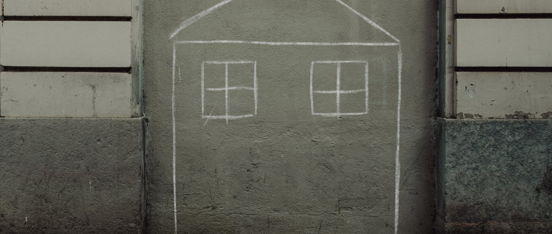 chalk outline drawing of a house on the side of a grey building