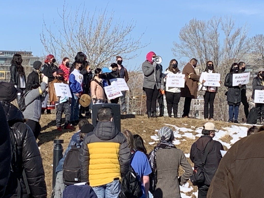 Several people attending an anti-racism rally outside. Woman wearing a hijab standing on a hill speaking to the crowd with a bullhorn.