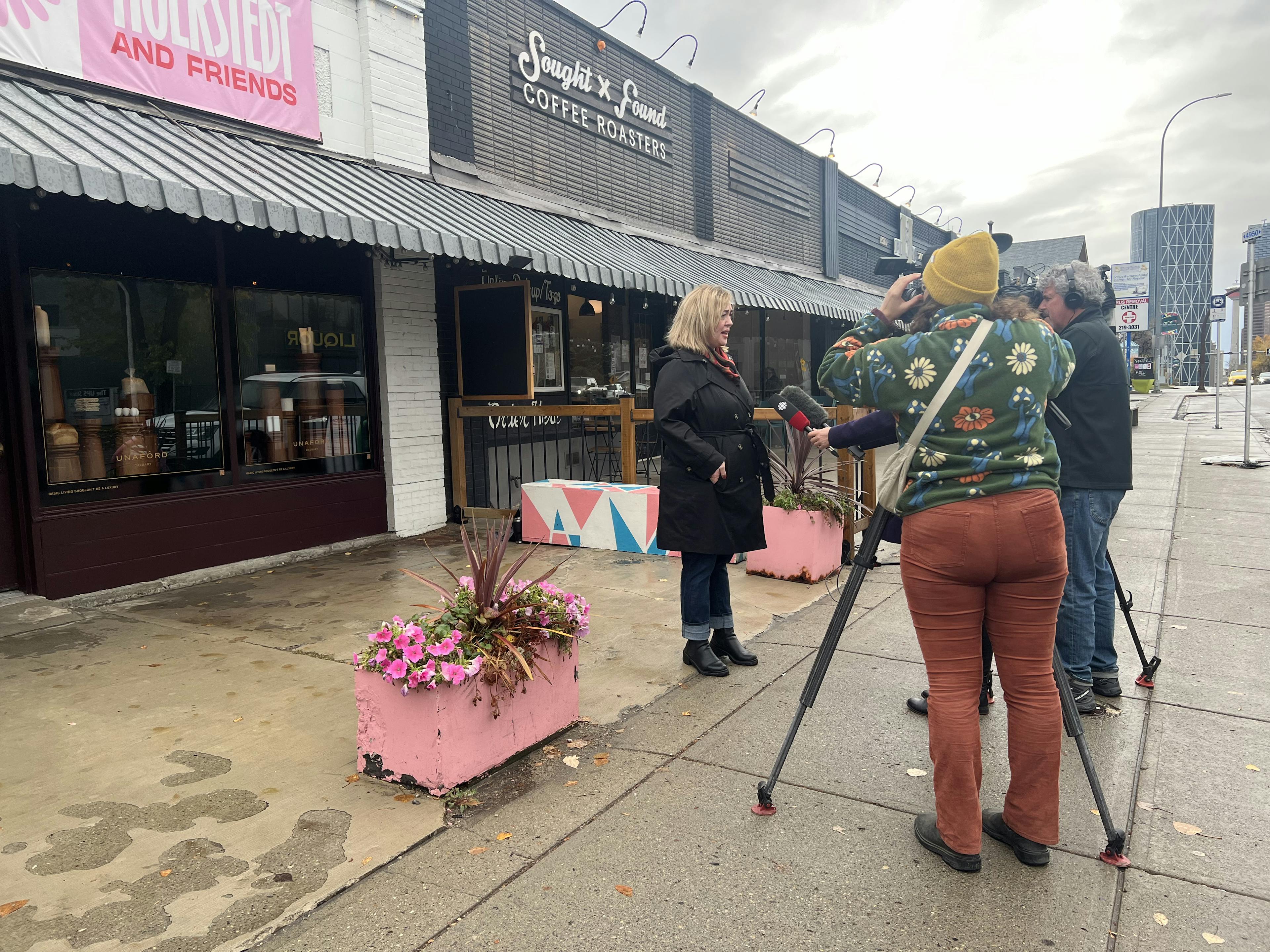 Reporters with cameras interviewing a woman in front of a storefront