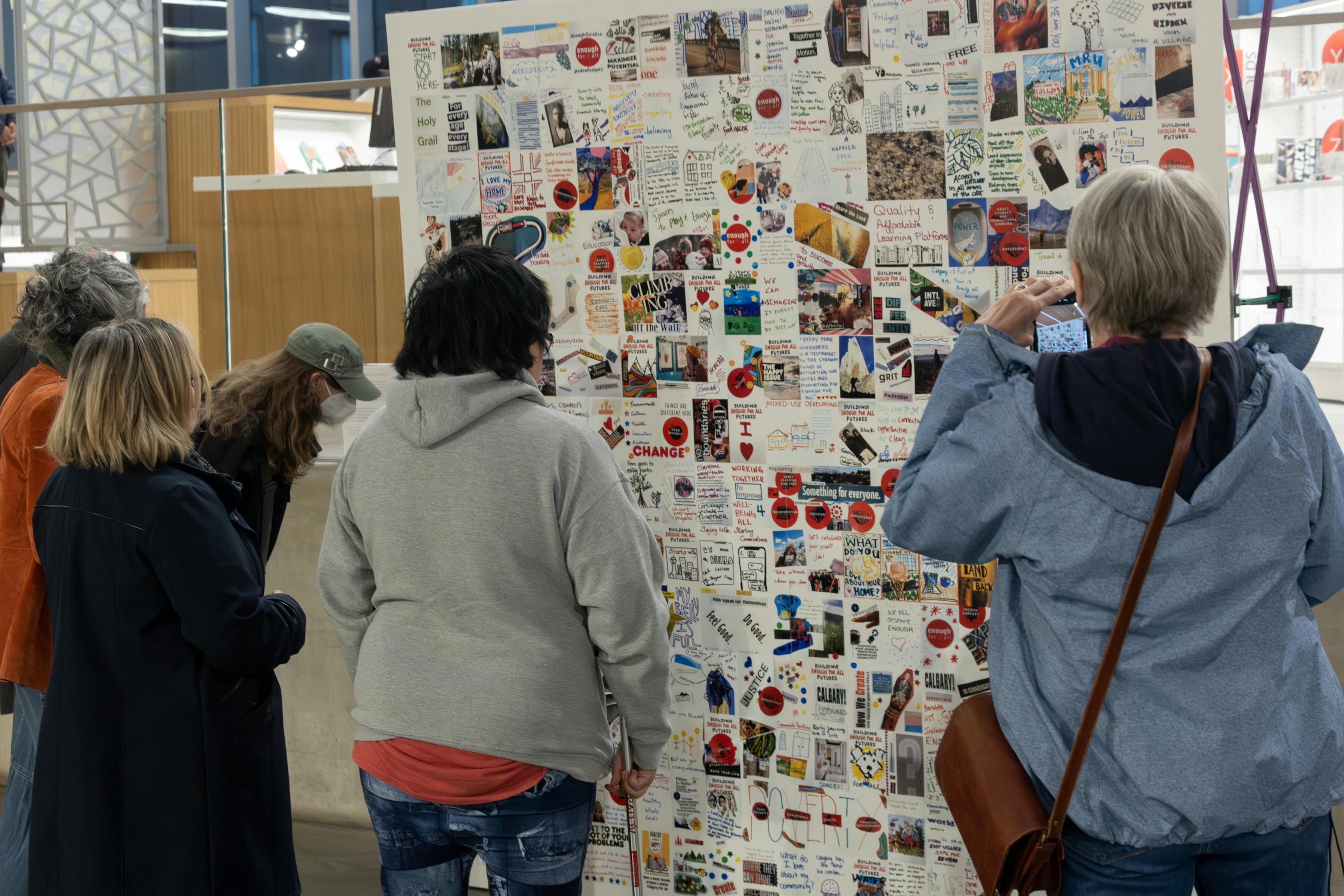 Three people with their backs to the camera looking at a zine collage mural