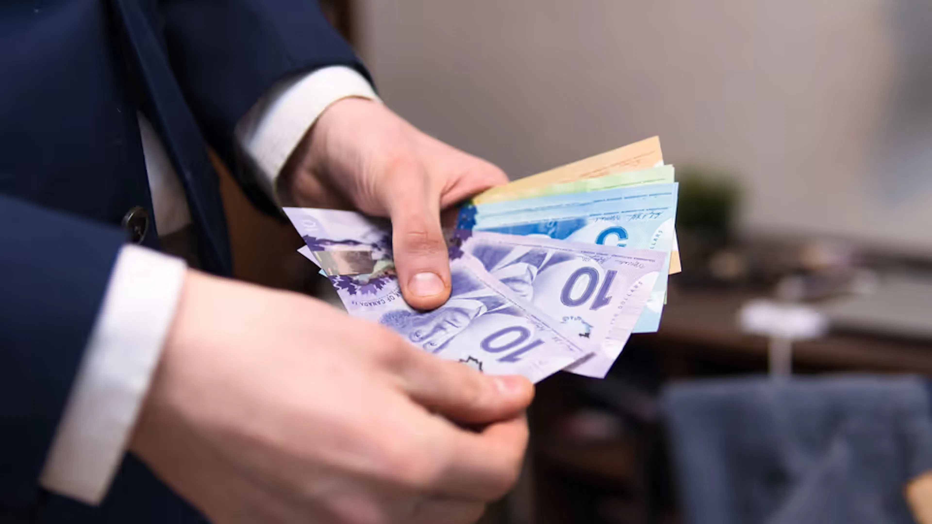 A white man in a navy blue suit counting Canadian dollars.