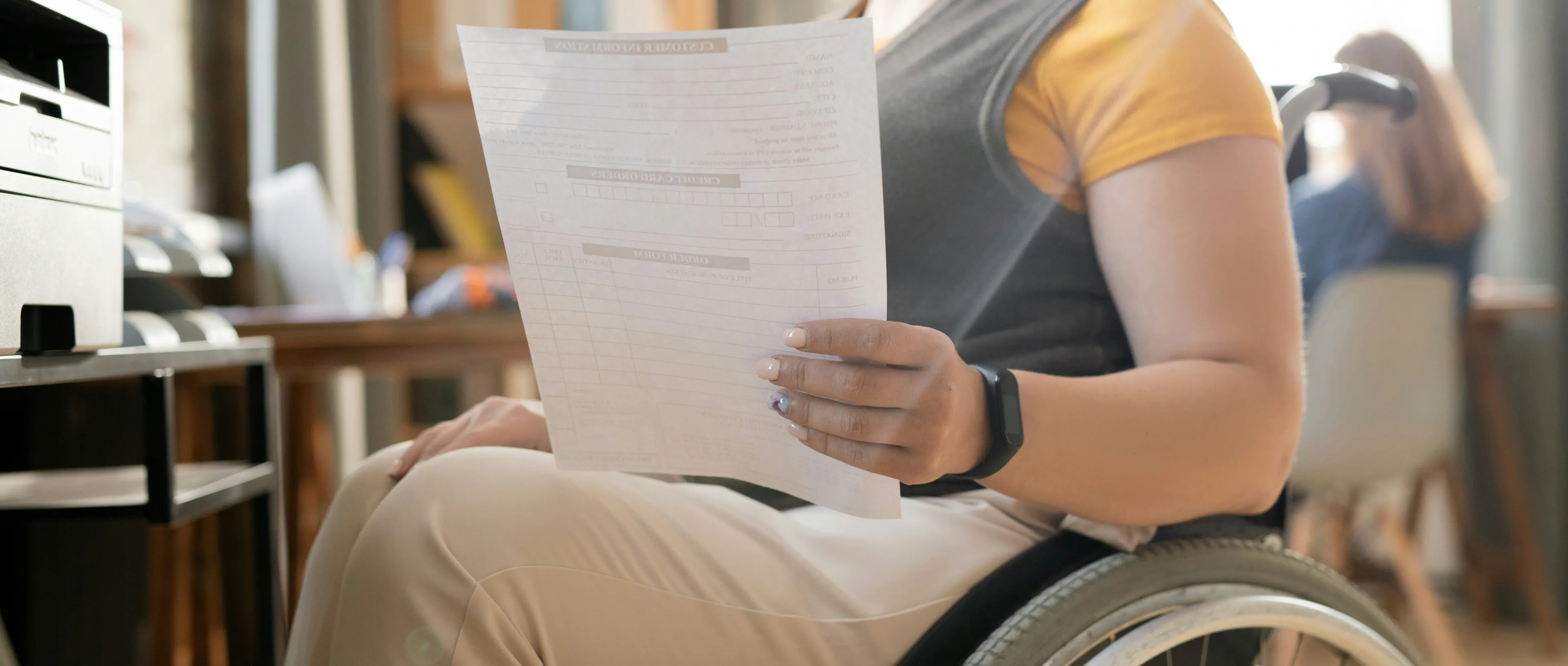 A woman is sitting in a wheelchair and holding up a piece of paper. 