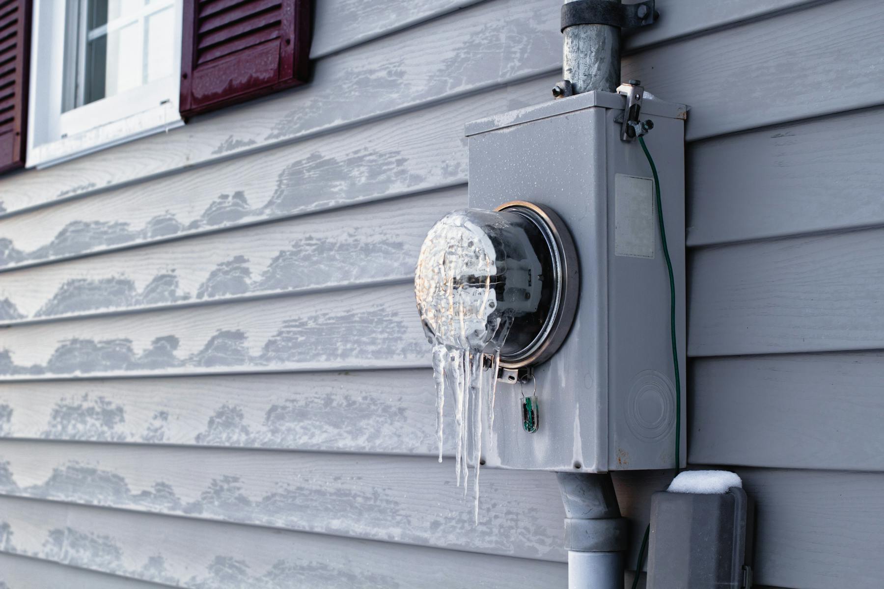Utility meter on the side of a house with icicles building on it.