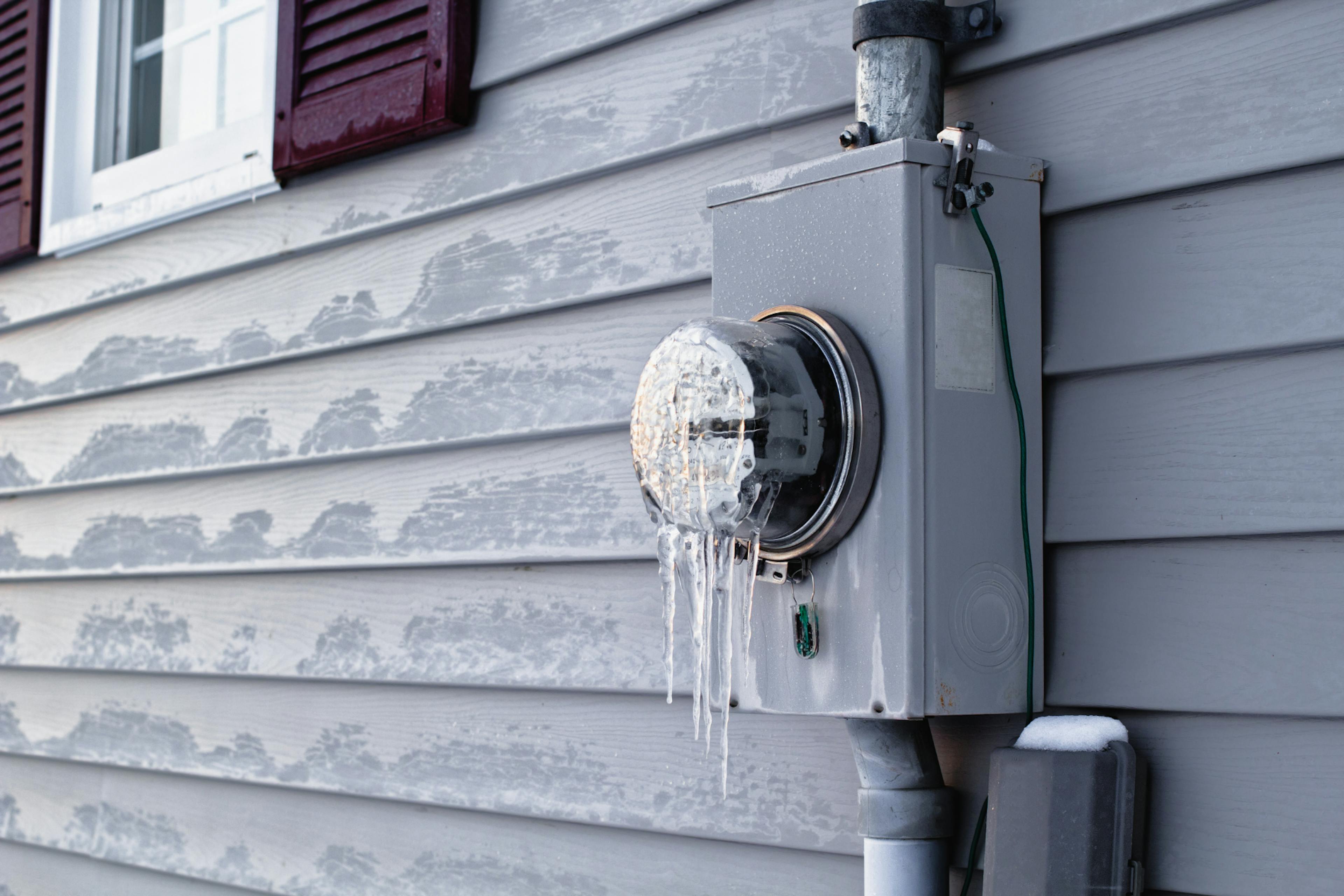 Utility meter on the side of a house with icicles building on it.