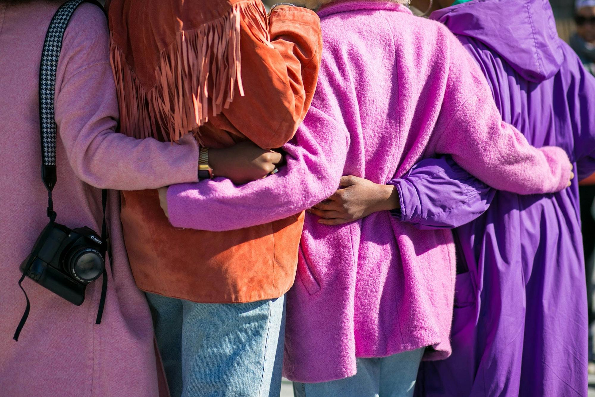 Four people in vibrant coats with their arms around each other