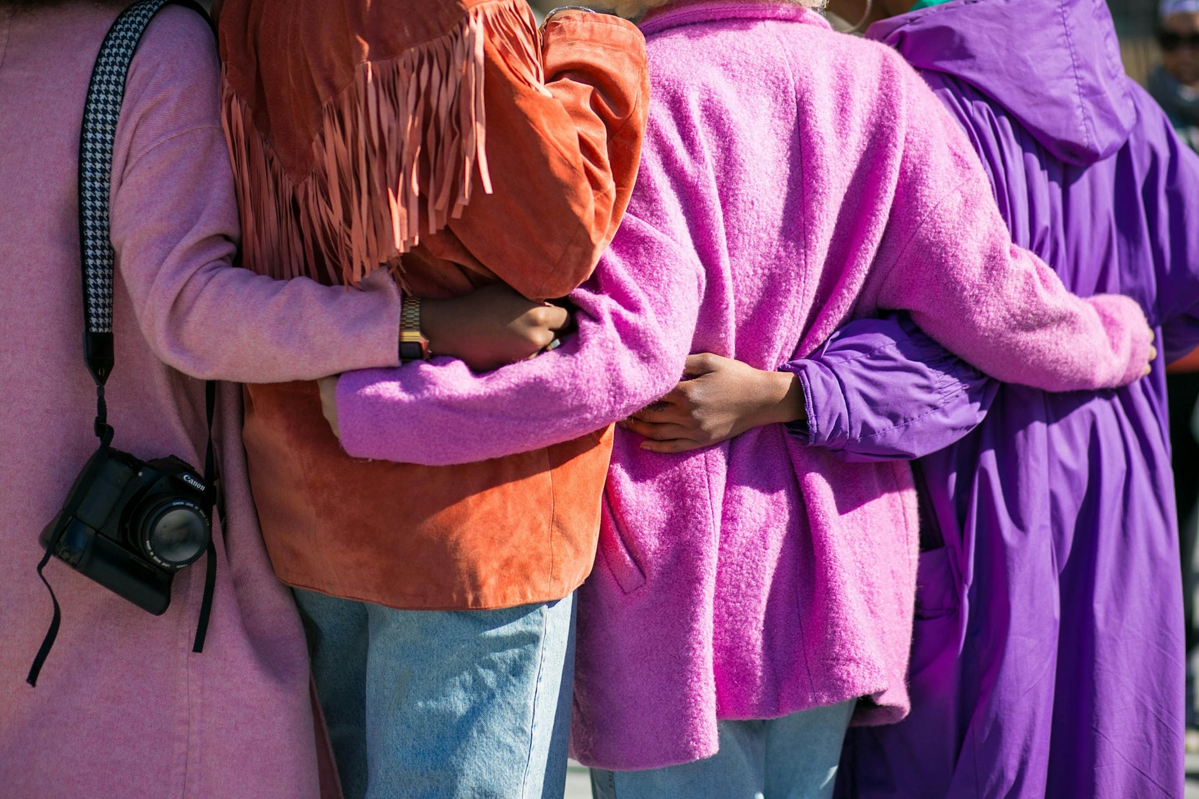 Four people in vibrant coats with their arms around each other