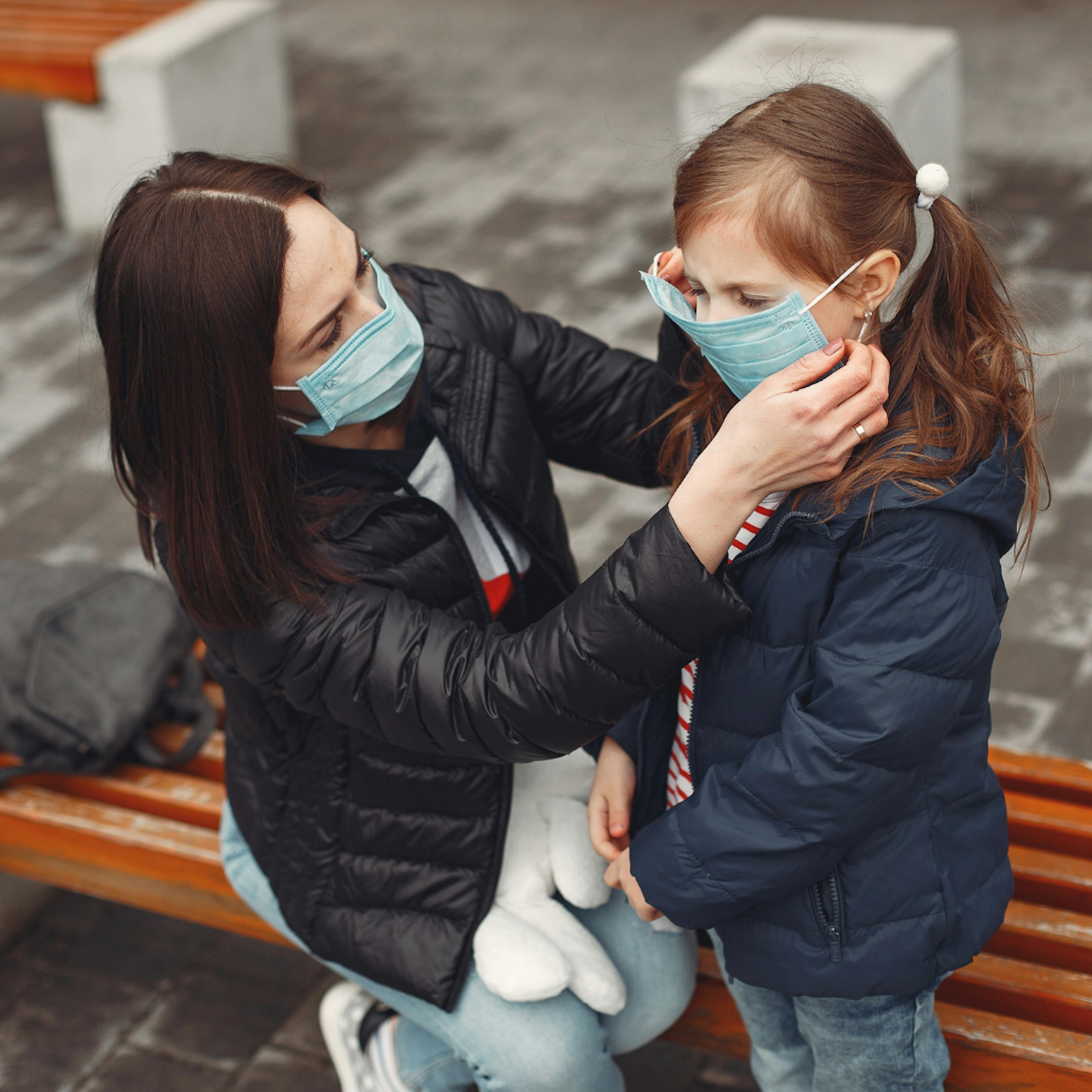 Woman helping her young daughter with a COVID-19 mask