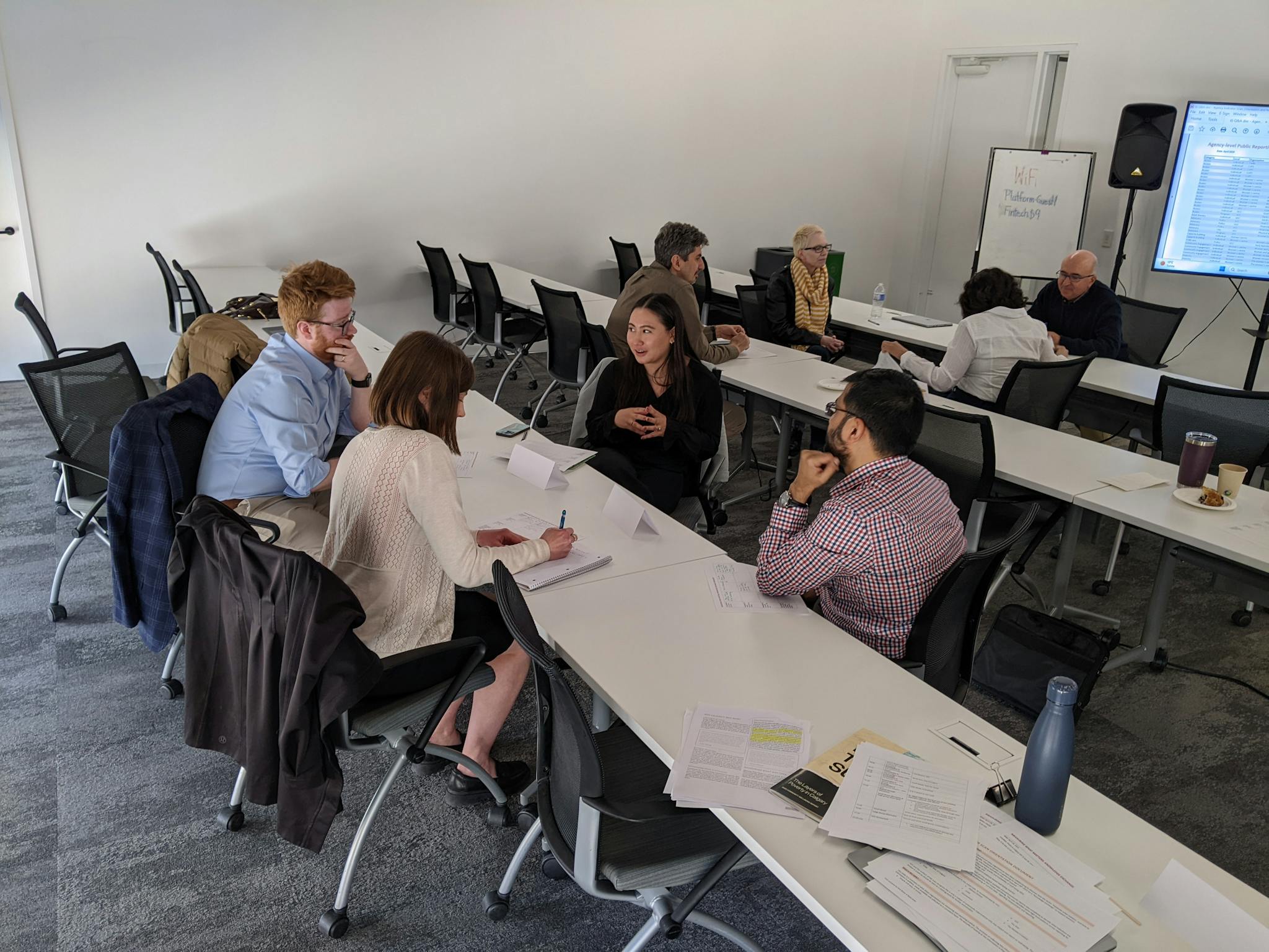 Four people sitting at a long table in a university classroom having a conversation.