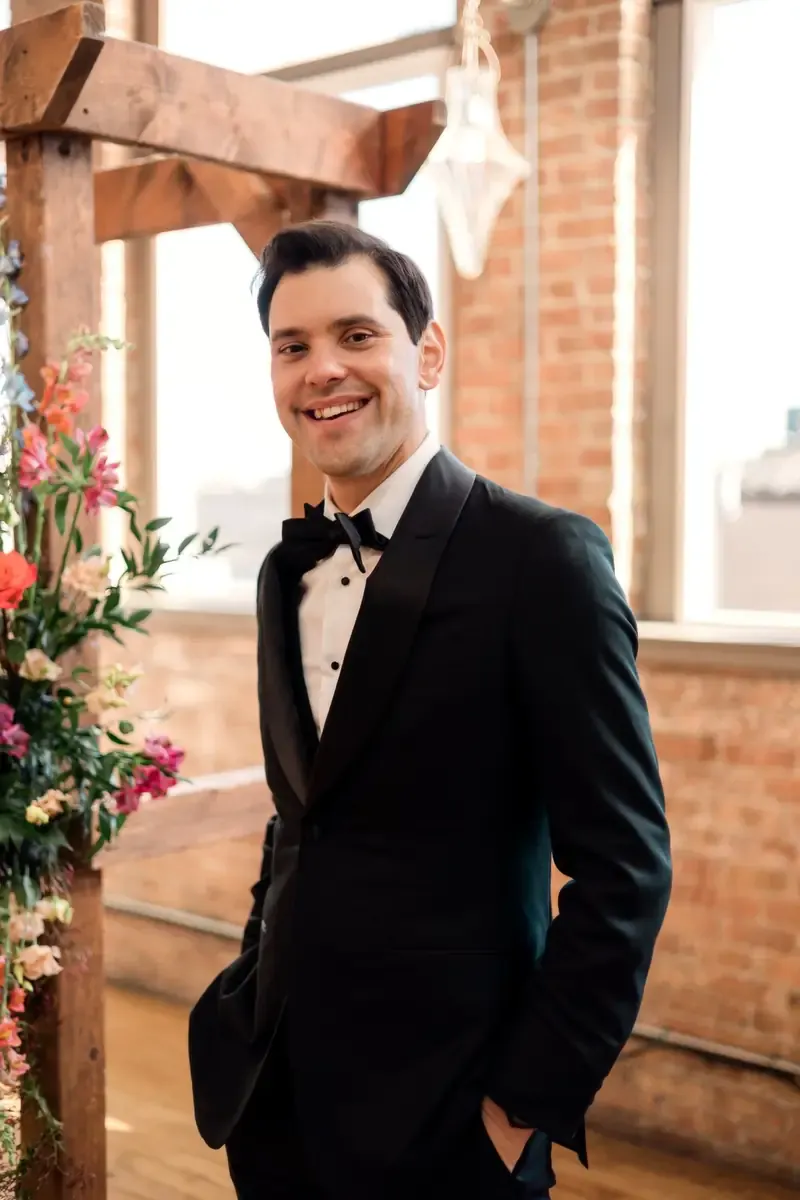 Ryan McCarthy in his custom Enzo Custom black tuxedo, smiling at the ceremony arch