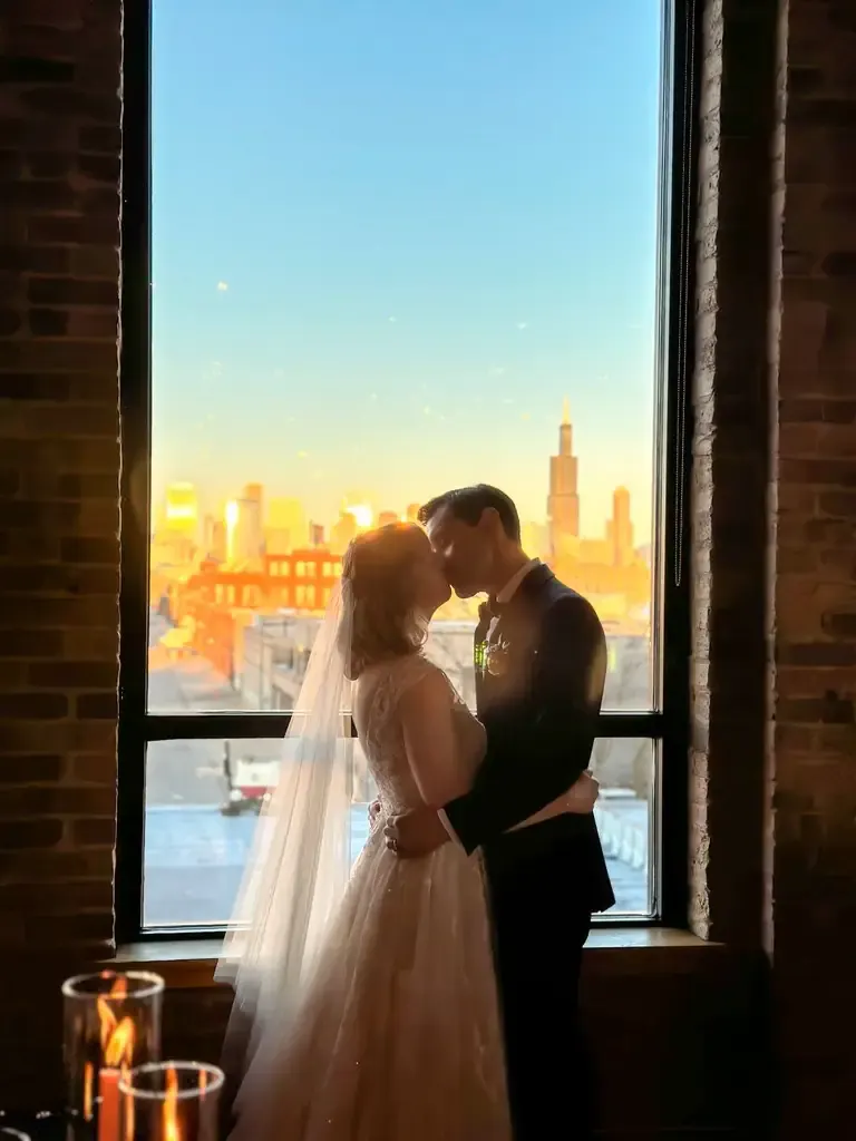 Ryan and Caroline kissing in front of a panoramic skyline window at golden hour