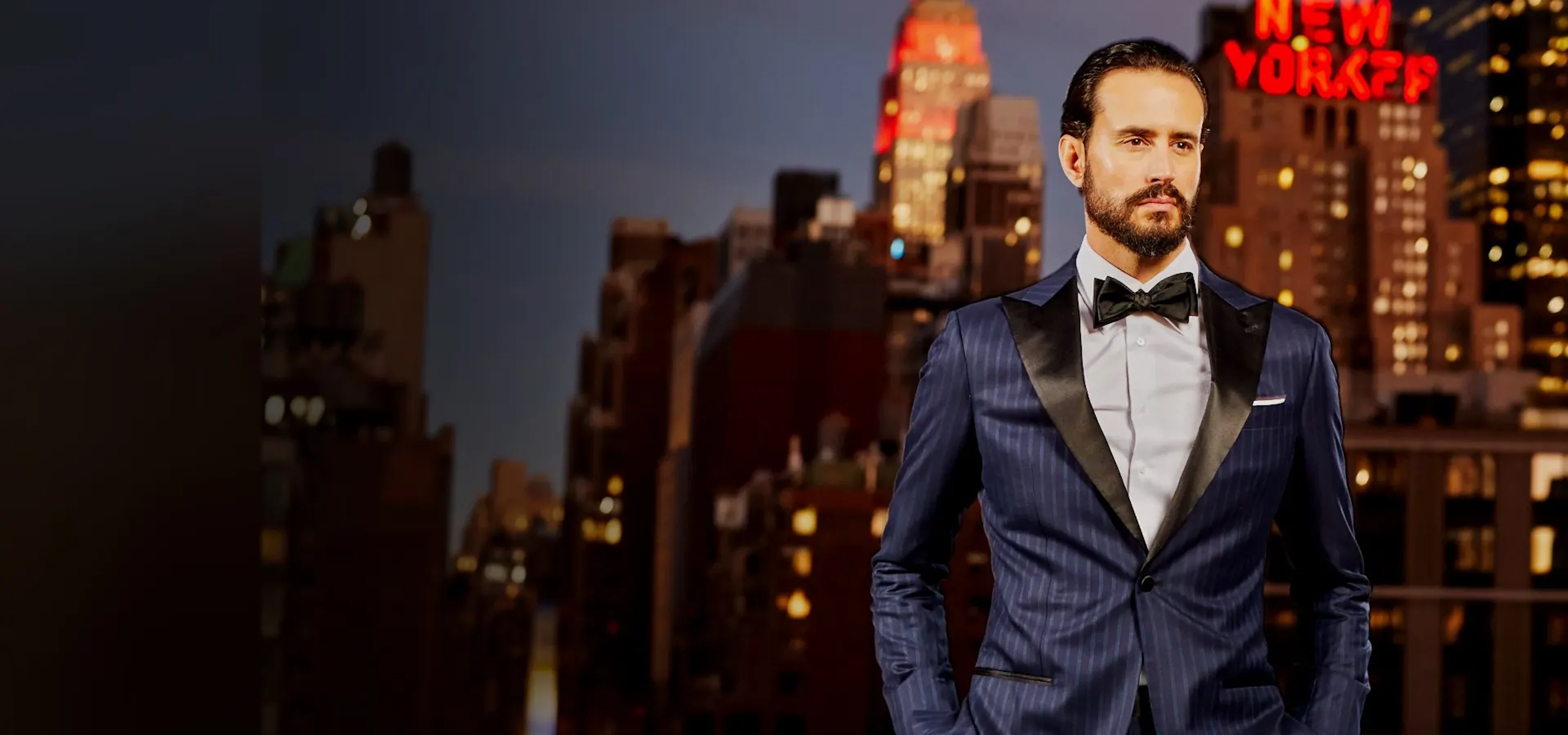 Custom midnight-navy pinstripe tuxedo with black satin peak lapels at night, Empire State Building behind