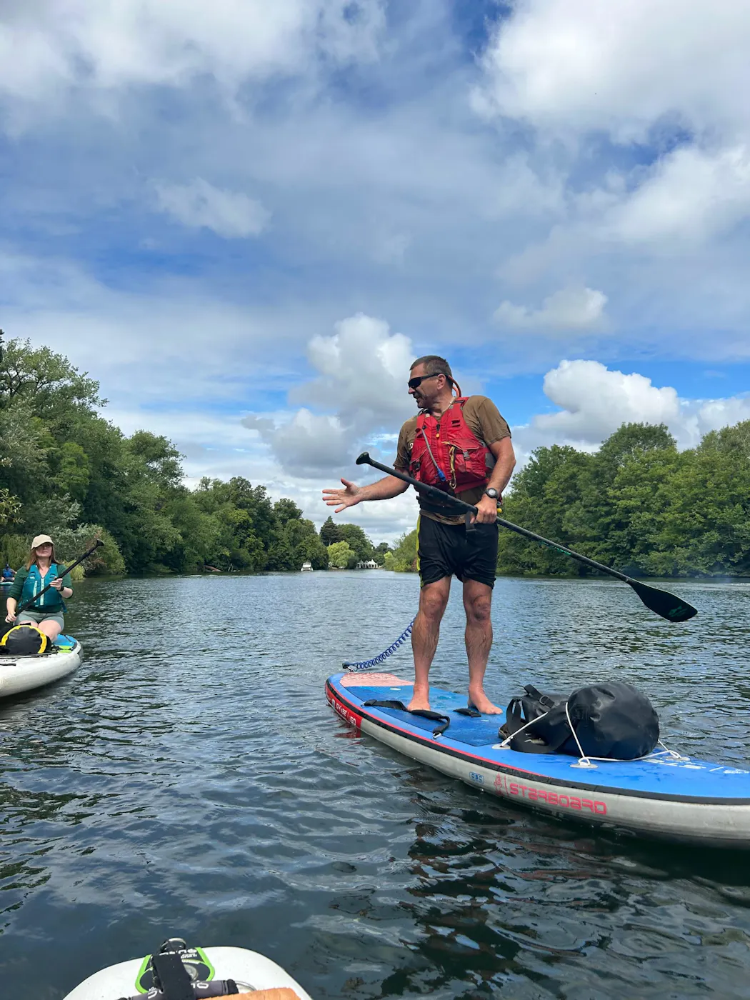 A paddleboard guide standing on his board leading a group along a wide stretch of the River Thames