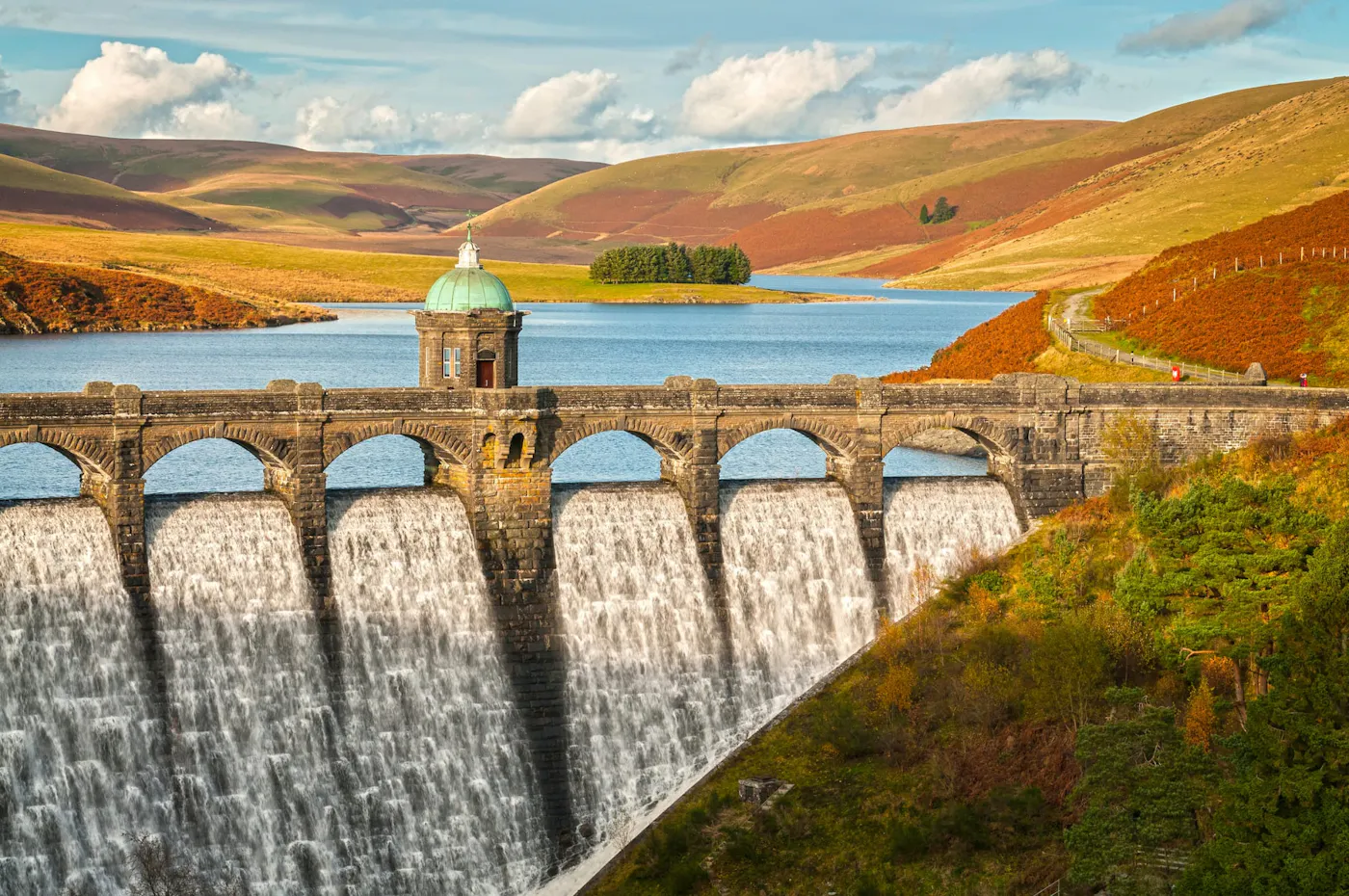 Water cascading over a Victorian dam in the Elan Valley, with a reservoir and hills behind