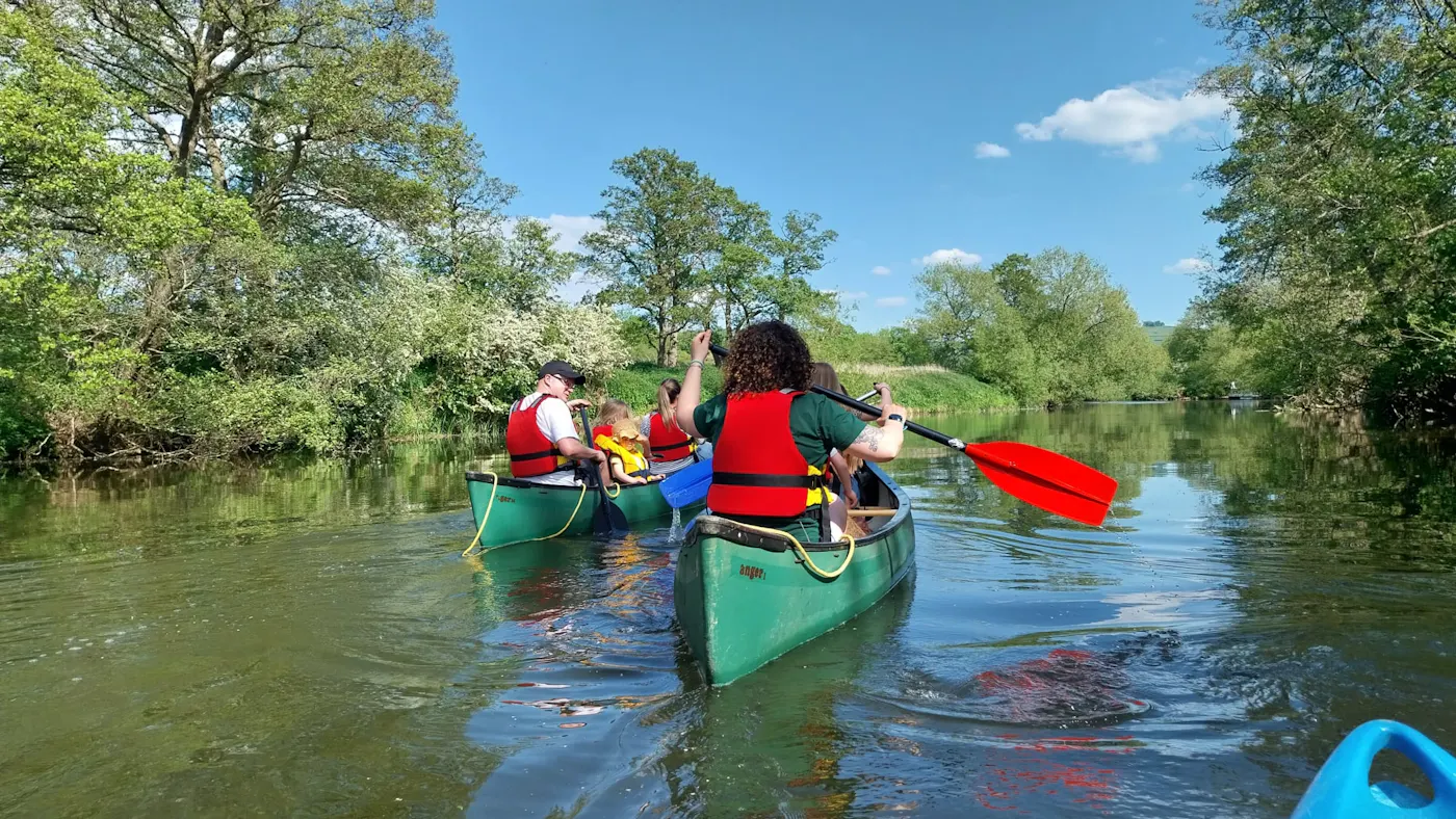 Paddlers in open canoes on a tree-lined stretch of the River Avon near Keynsham