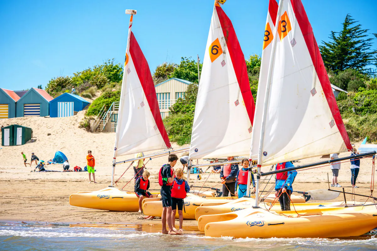 Sailing dinghies lined up on Abersoch beach with young sailors in buoyancy aids