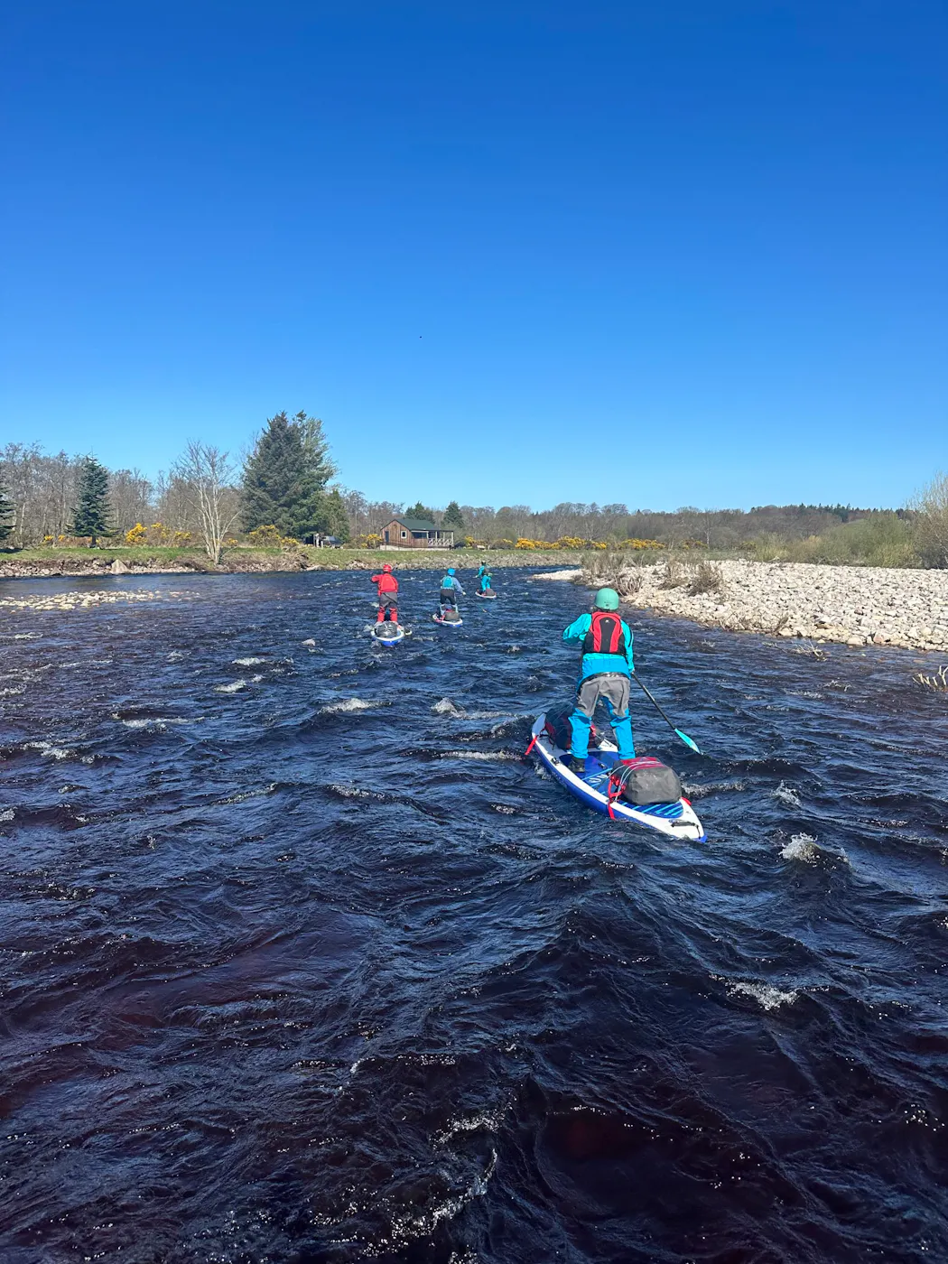 Paddleboarders with laden expedition boards paddling down a fast-flowing stretch of the River Spey