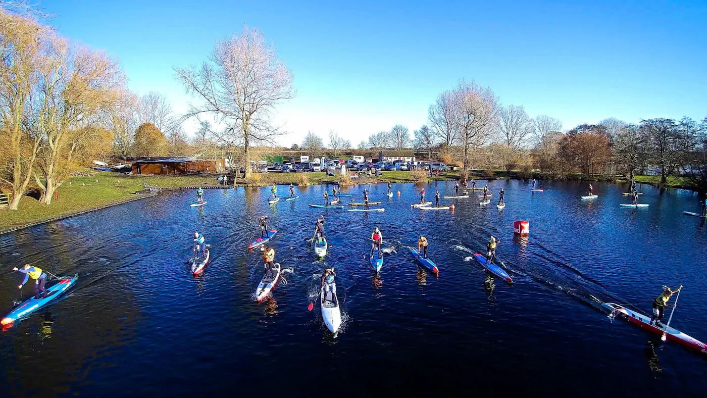 A large group of stand-up paddleboarders out on a lake on a bright, sunny day