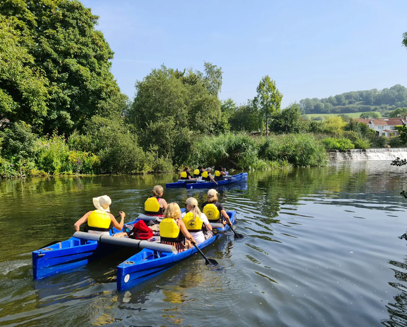 Groups in buoyancy aids paddling blue Katakanu canoes on the River Avon near Bath