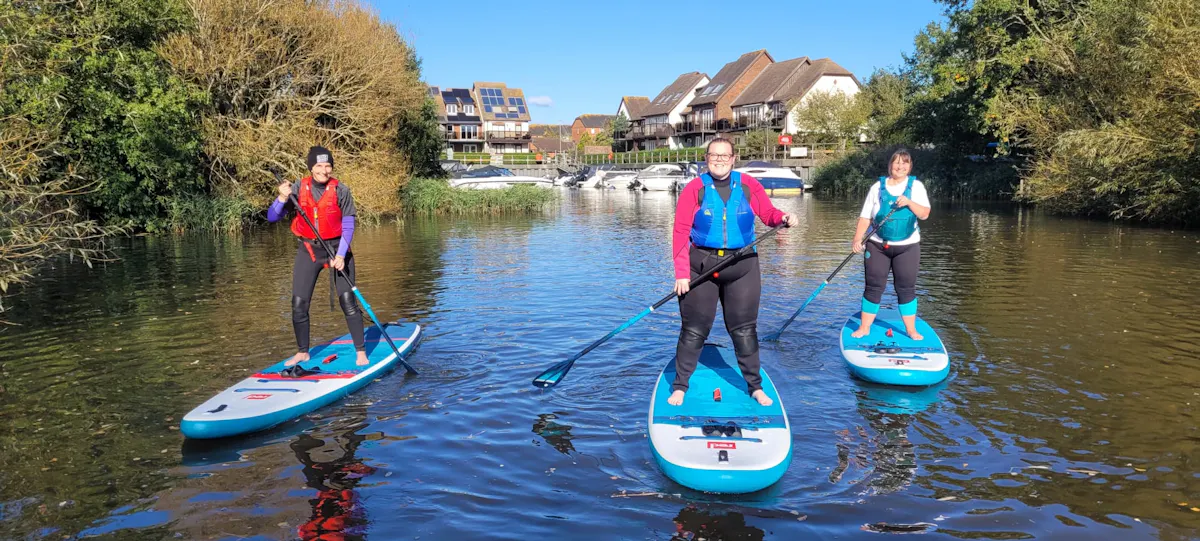 Three paddleboarders standing on their boards on a calm river on a sunny day