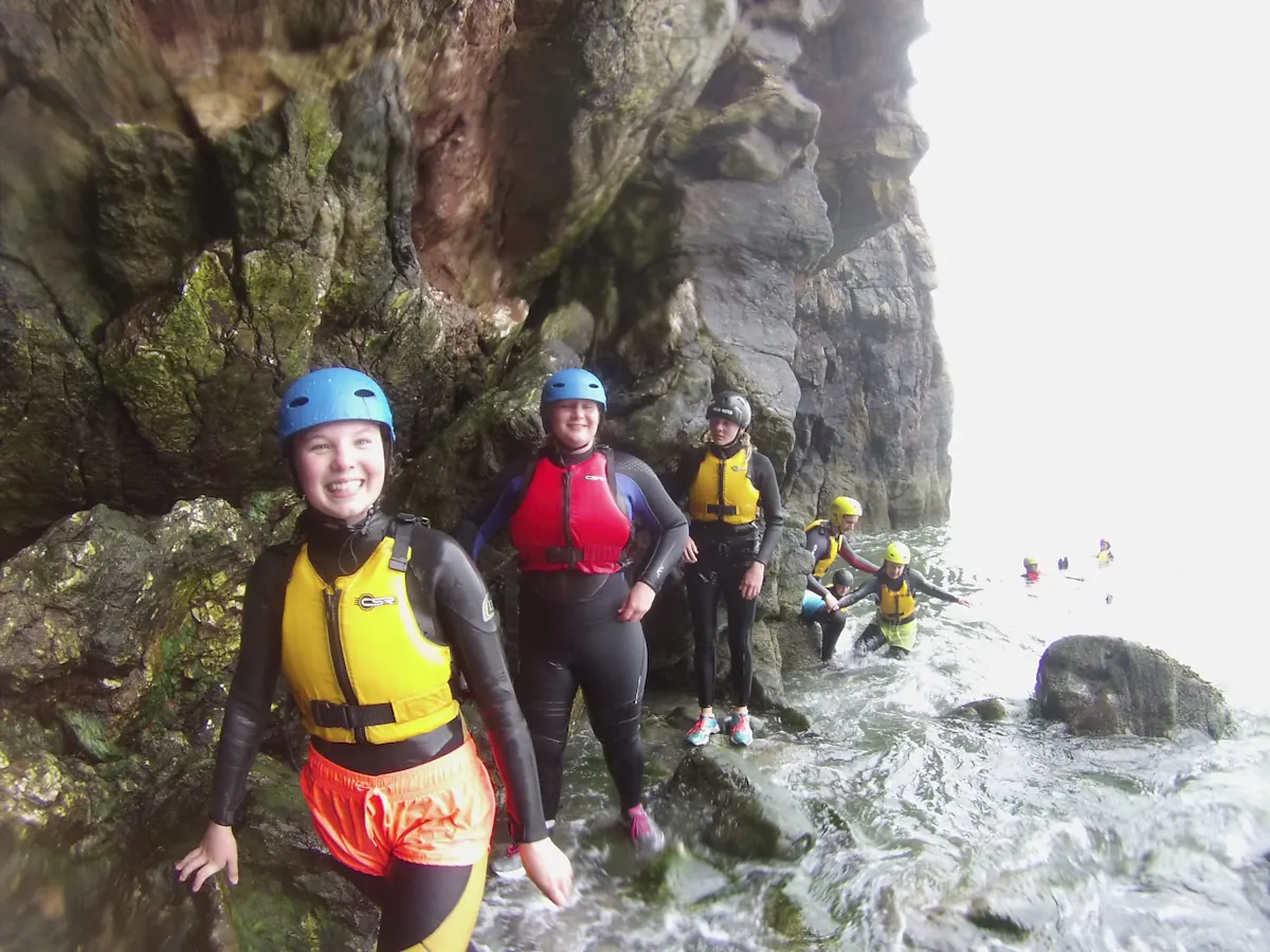 A group in wetsuits, helmets and buoyancy aids among the rocks at the foot of sea cliffs in South Wales